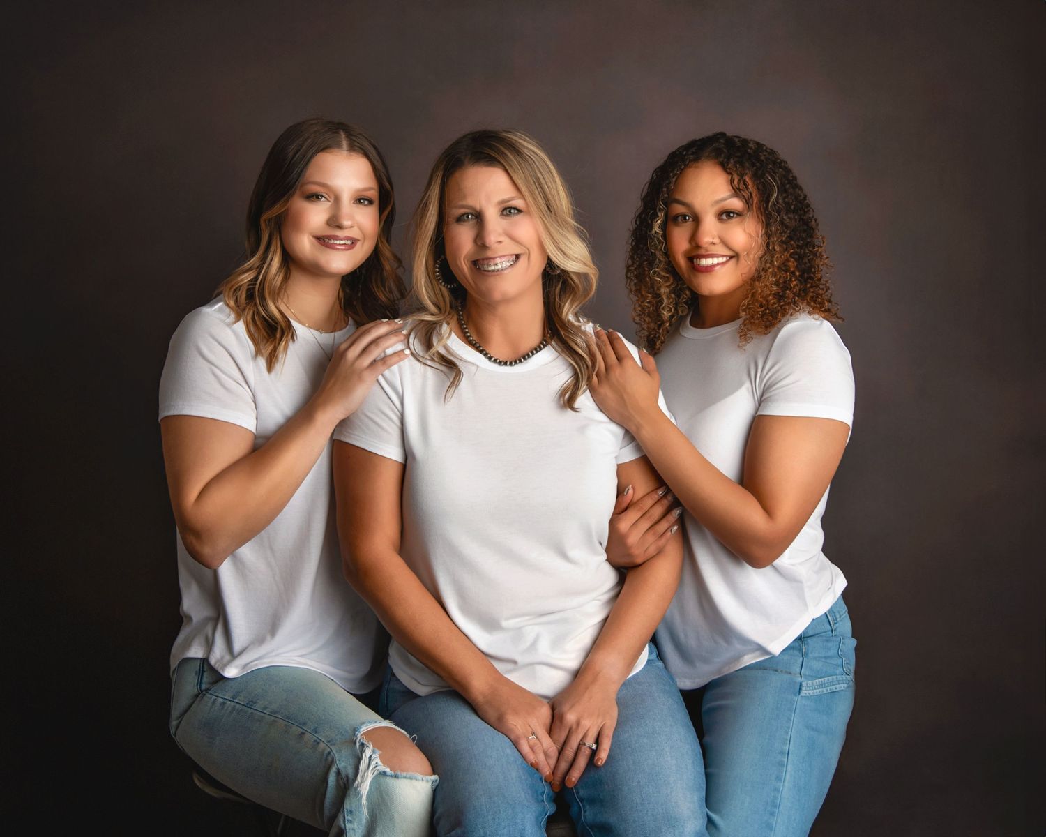 Three people in white t-shirts and jeans pose together for a studio portrait.