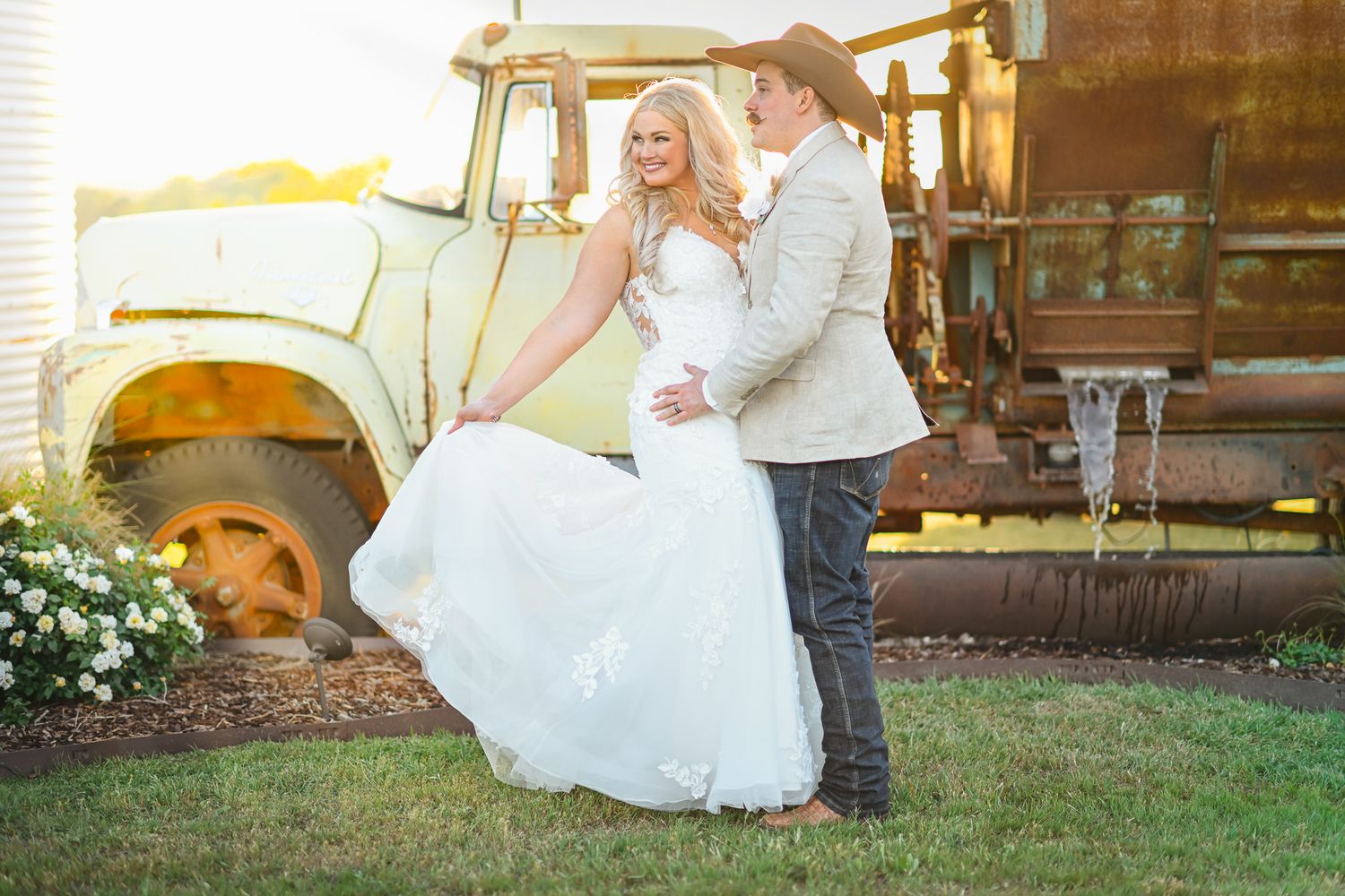 A romantic wedding photo near a vintage tractor at golden hour.