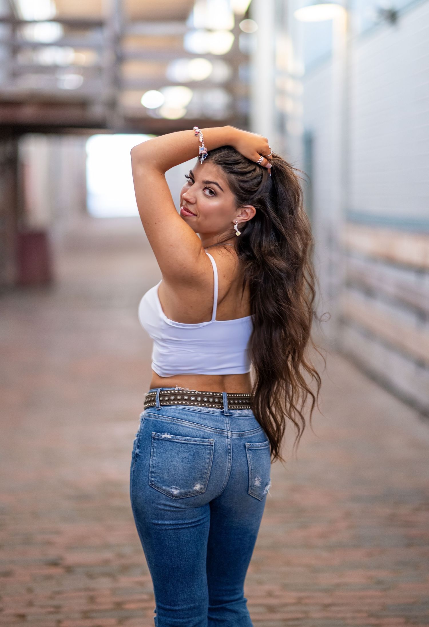 Person in white crop top and jeans poses while running hands through long dark hair.