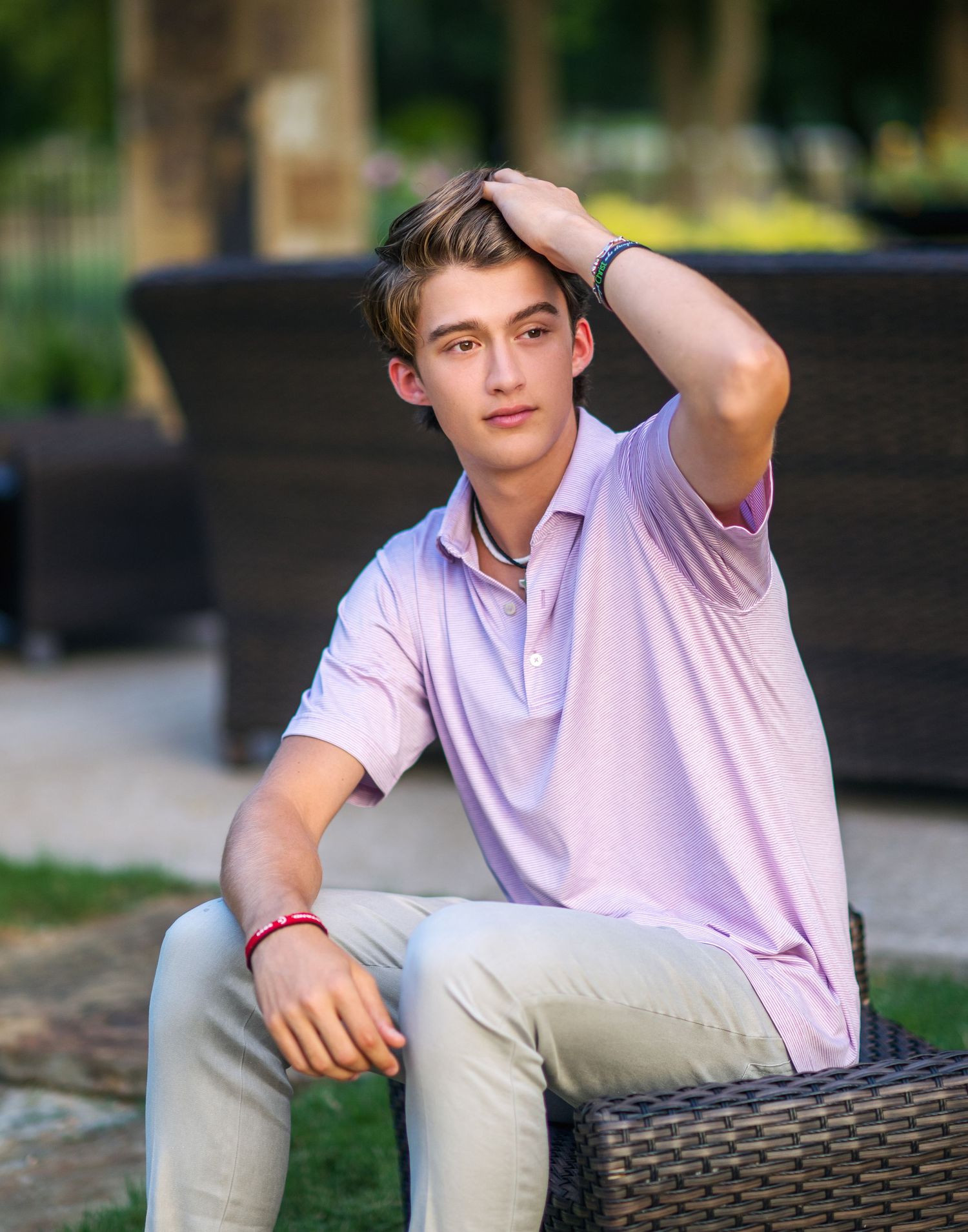 A casual outdoor photoshoot featuring someone in a light pink shirt and khaki pants sitting on wicker furniture.