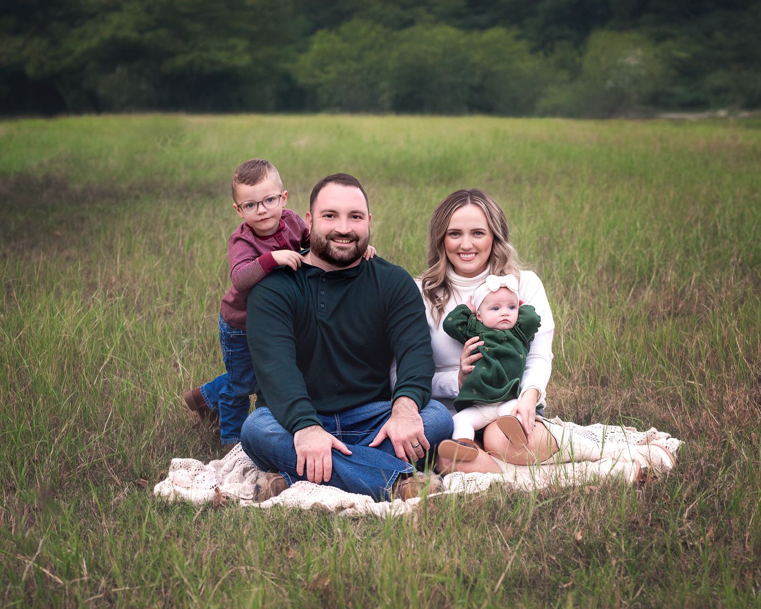 Family relaxing on blanket in grassy field during outdoor photo session.