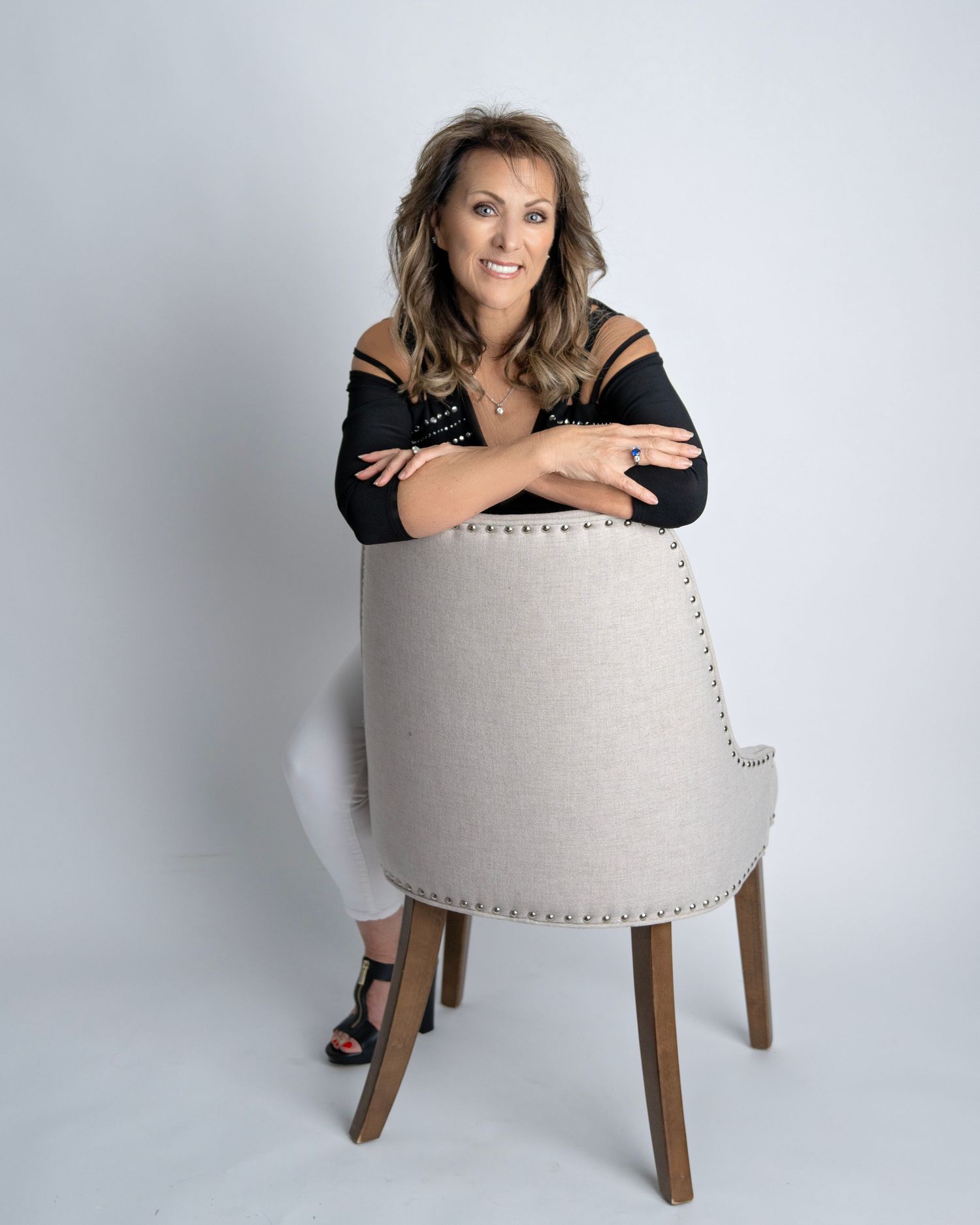 A creative portrait series showing someone posing playfully behind a white upholstered chair against a light backdrop.