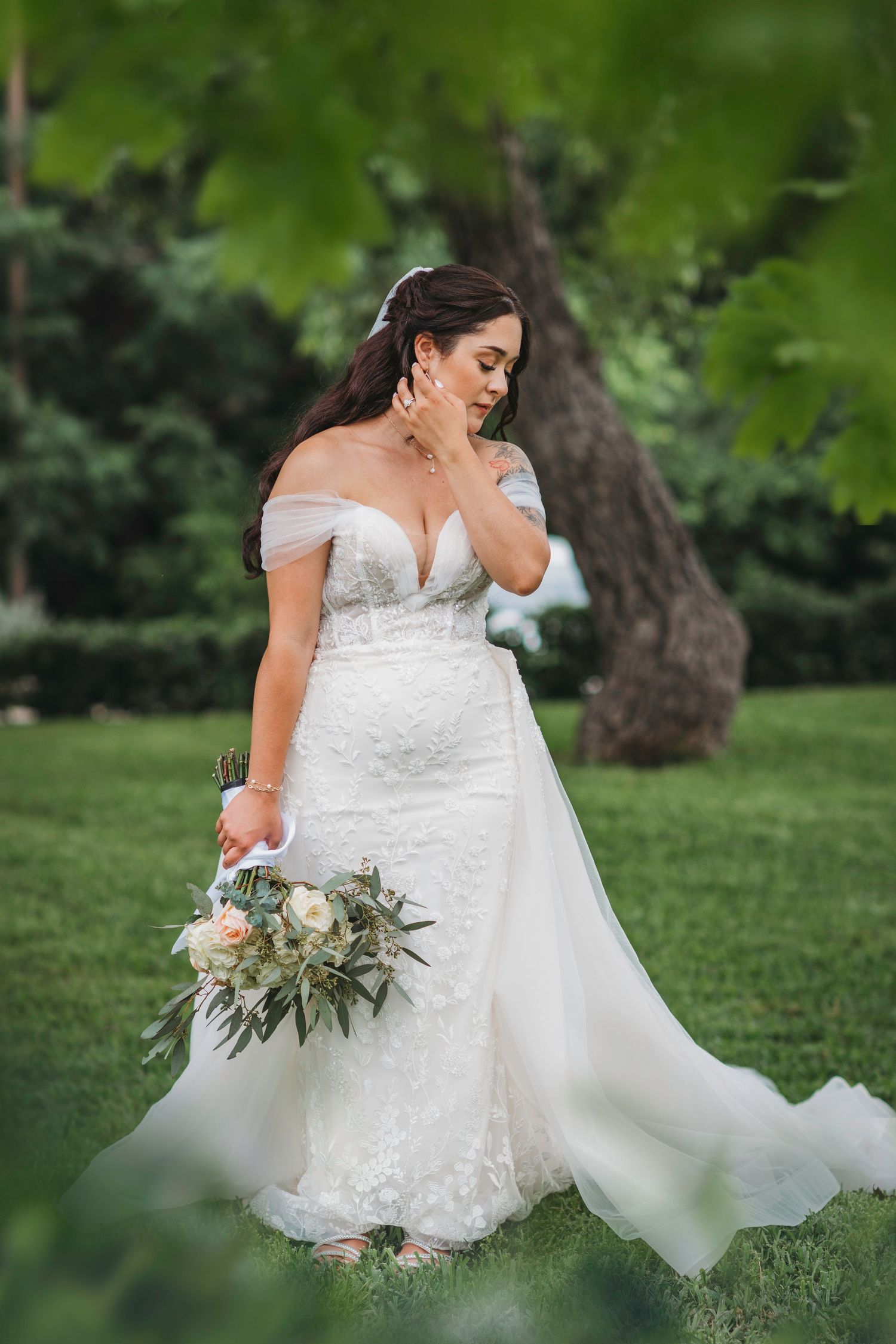 Beautiful off-shoulder lace wedding gown showcased in outdoor garden setting.
