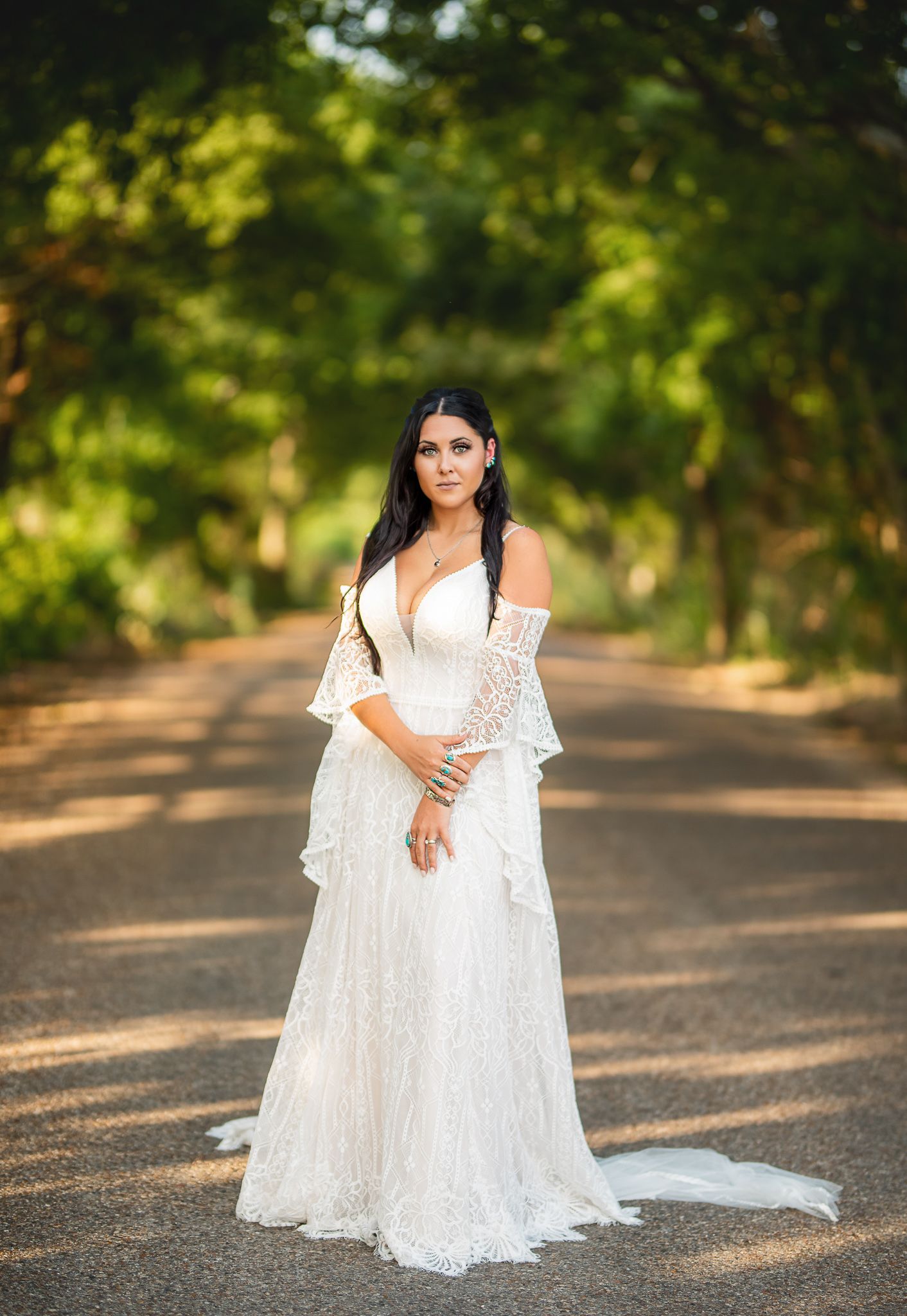 Long white lace dress with bell sleeves photographed on a tree-lined road.