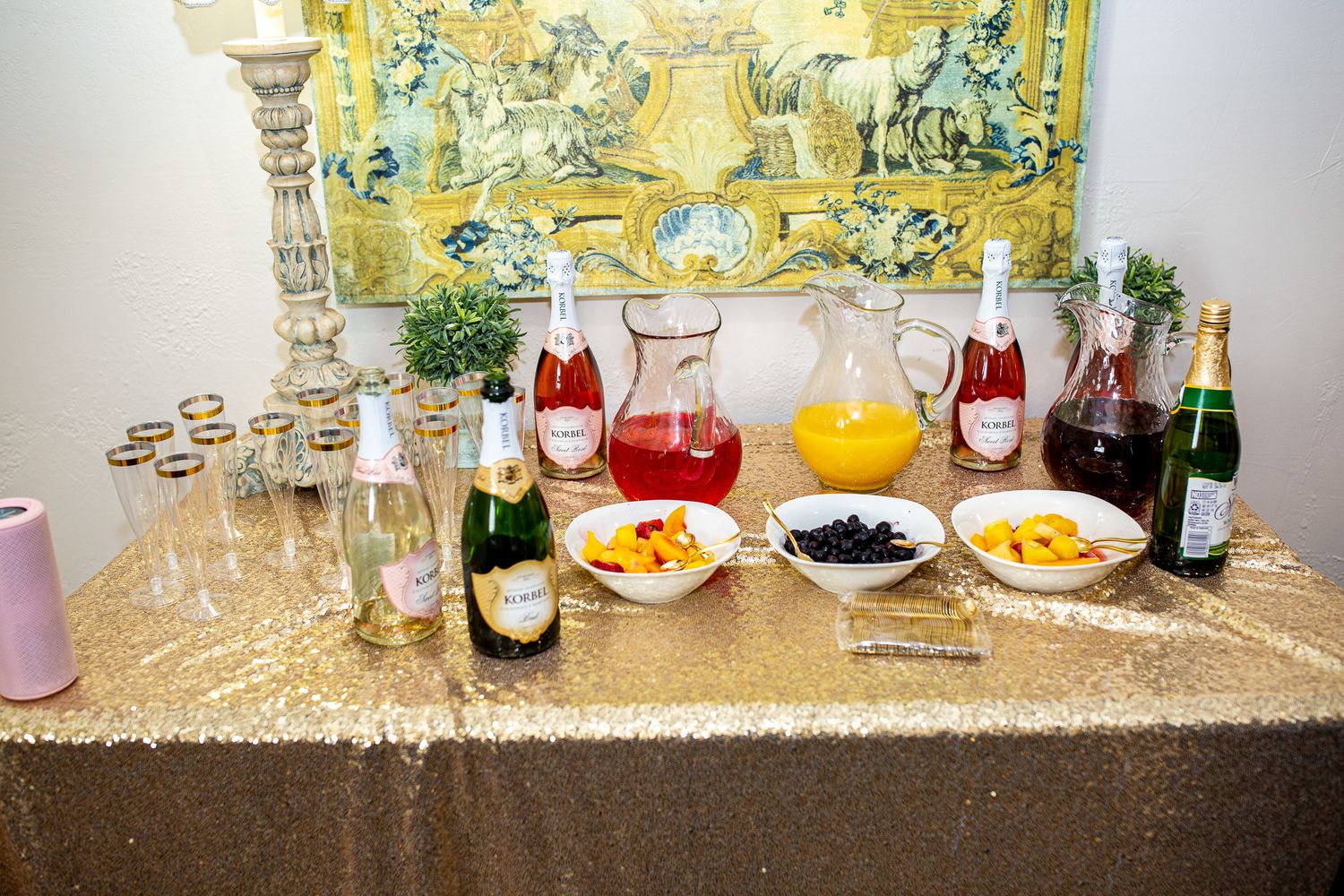 Mimosa bar setup with champagne bottles, juices and garnishes on sequined tablecloth.
