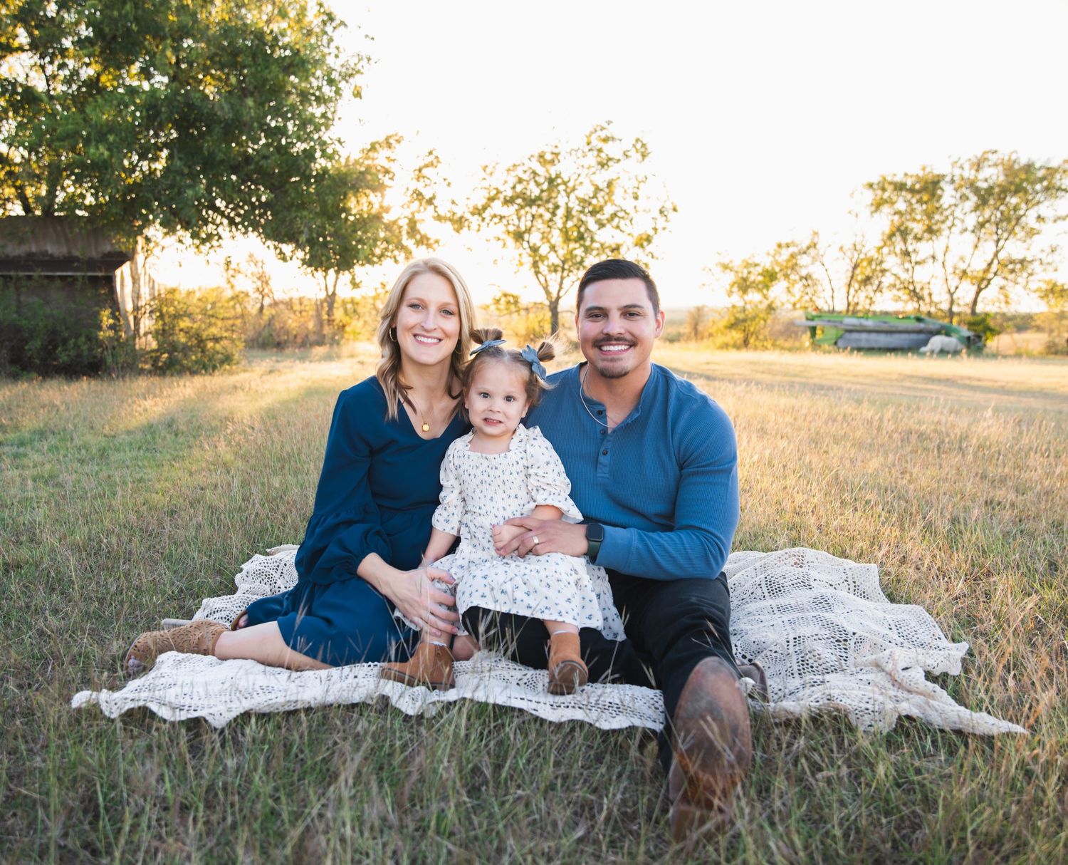 Family sitting together on blanket in grassy field during golden hour.
