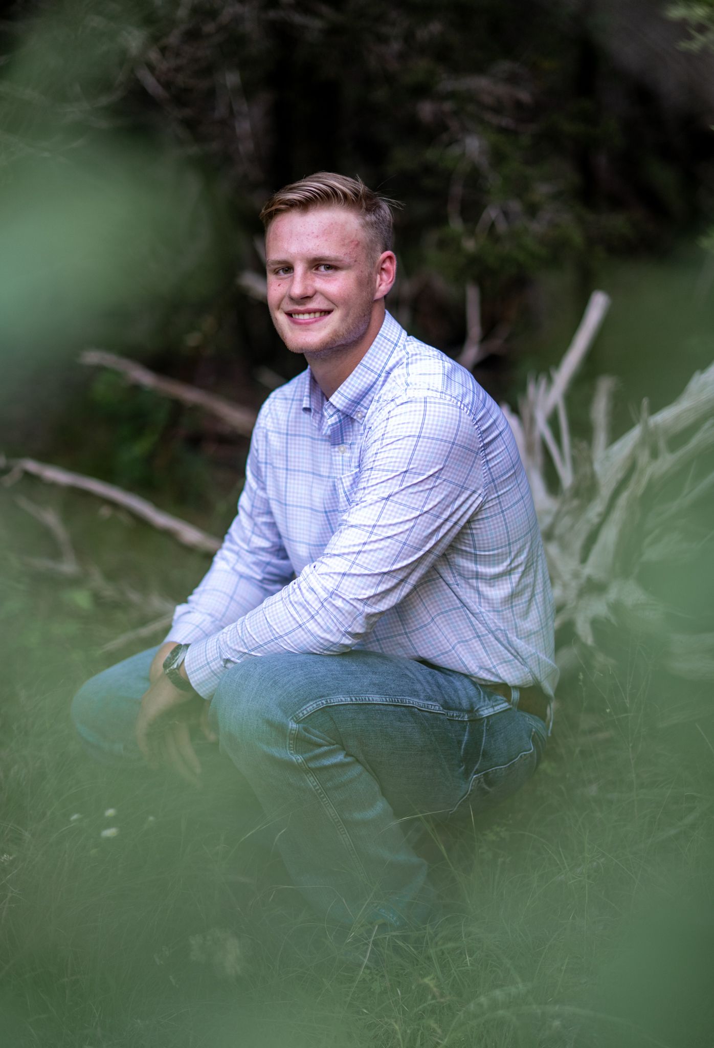 Professional senior portrait poses in lush green grass with white striped shirt and jeans.