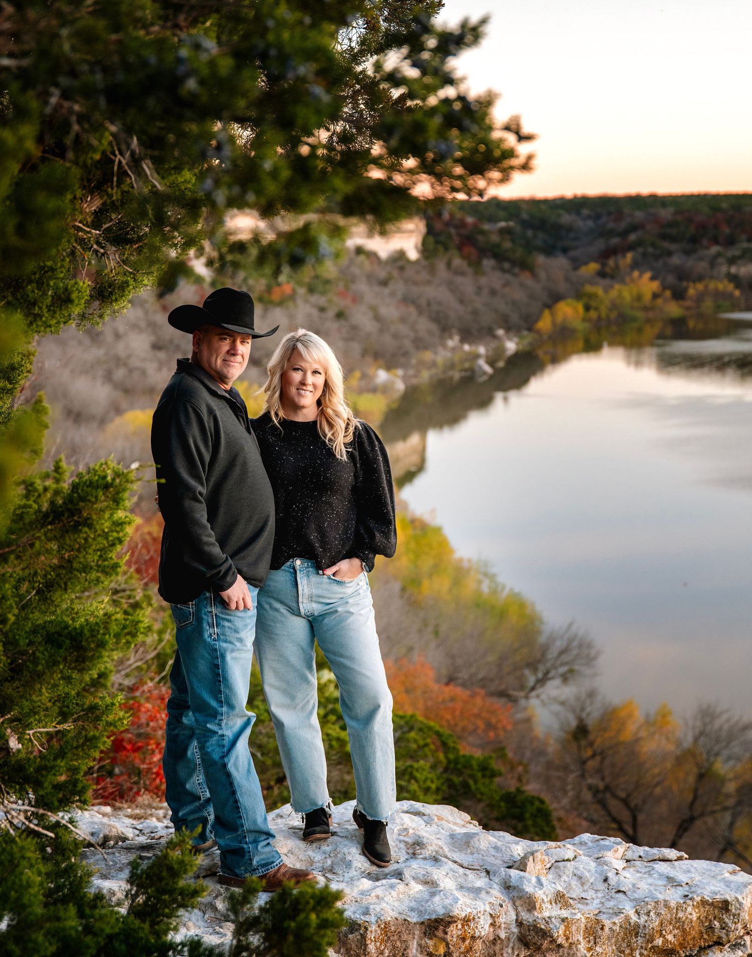Family photos captured on rocky cliff overlooking lake during golden hour sunset.
