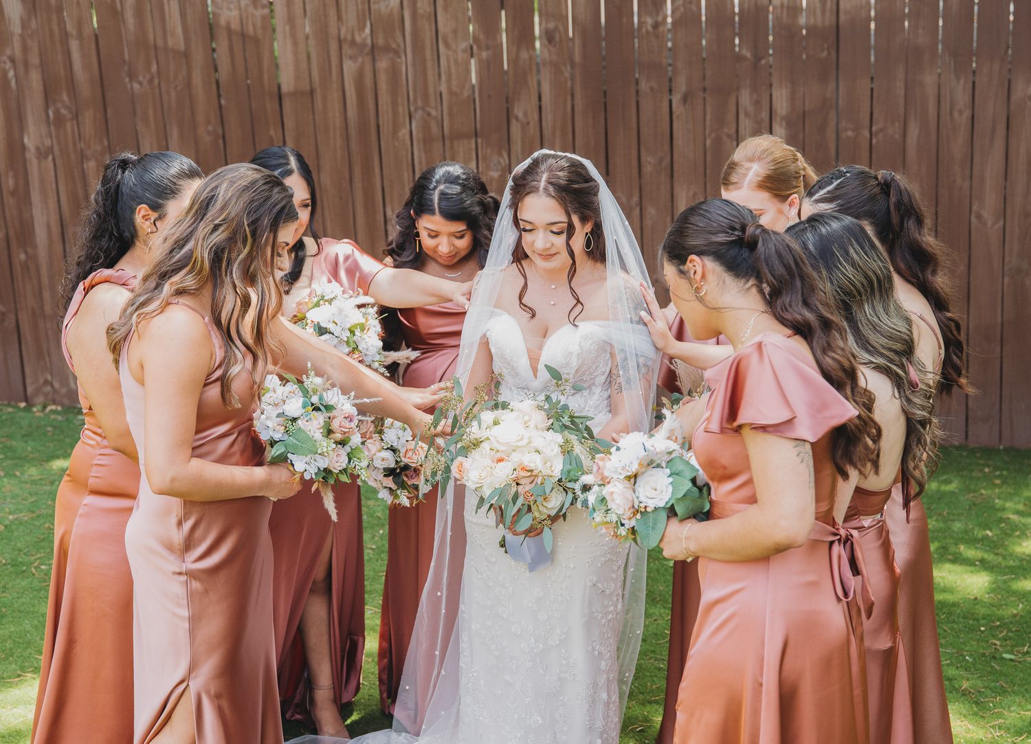 Bridesmaids in coral dresses gather around a bride in a backyard setting.