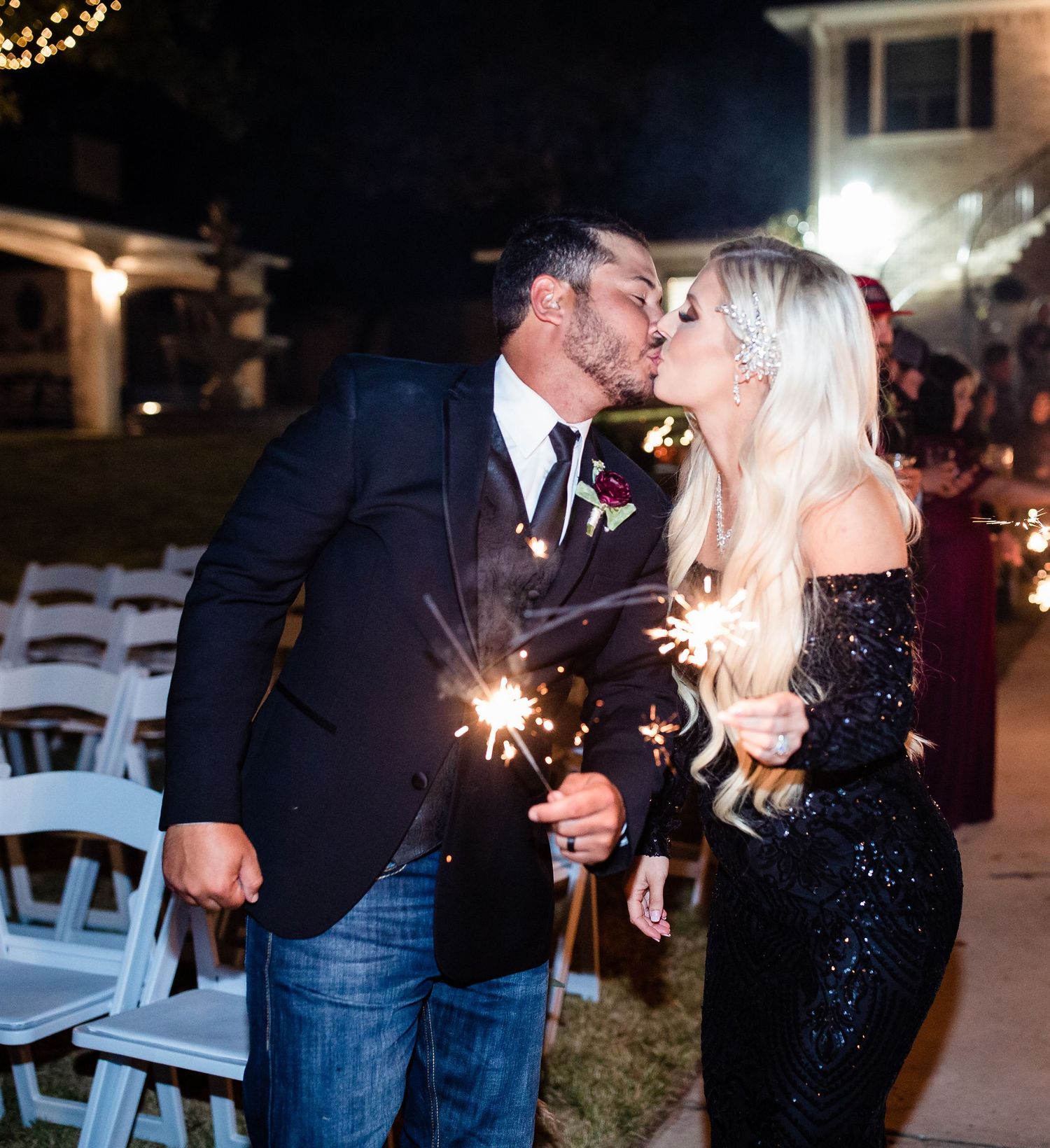 Couple shares romantic sparkler kiss during nighttime wedding celebration.