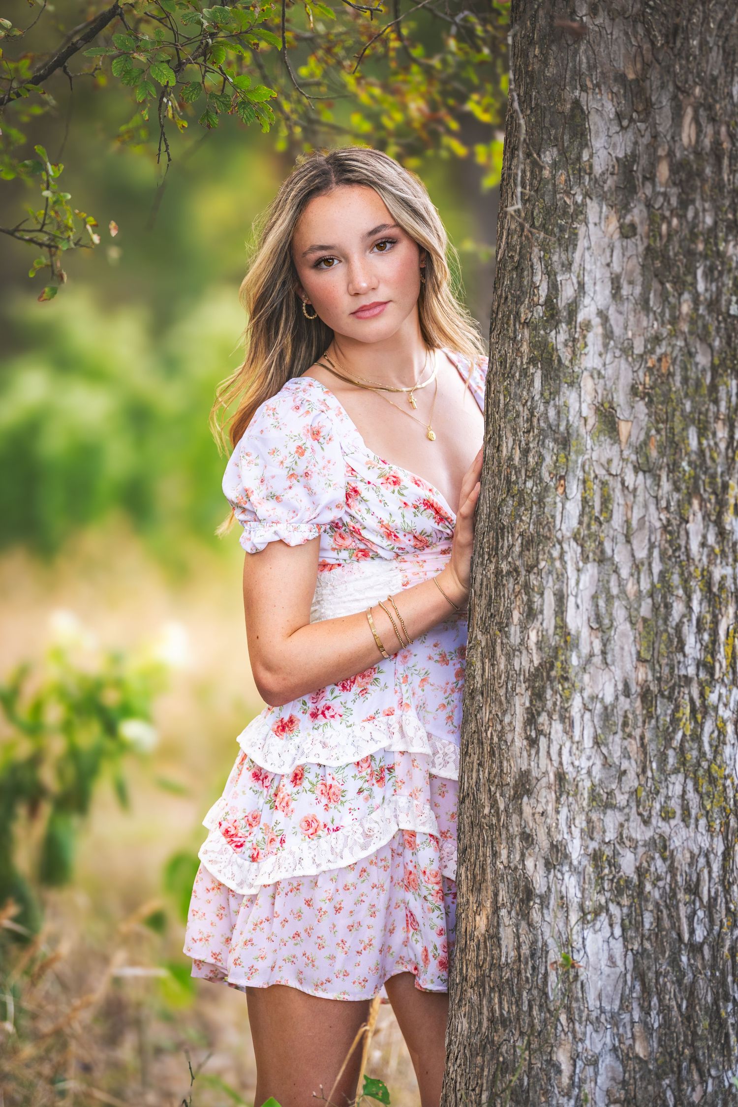 A series of outdoor portraits showing someone in a white and red floral dress posing against a tree trunk in natural lighting.
