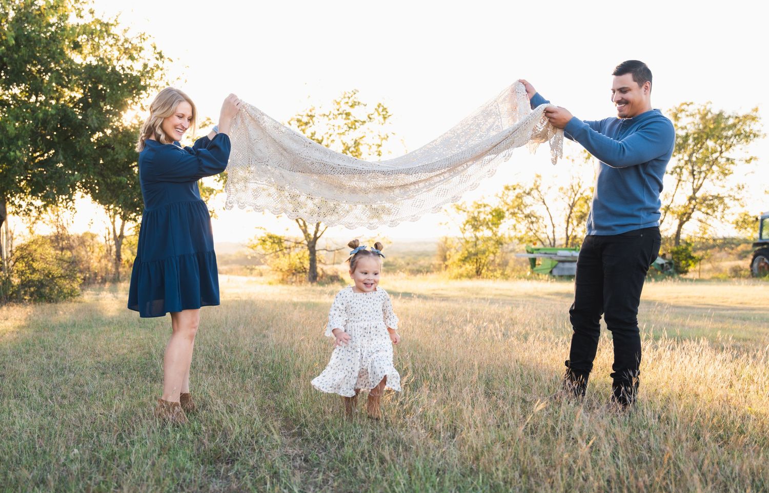 Family plays with white fabric in sunlit field during sunset photo session.