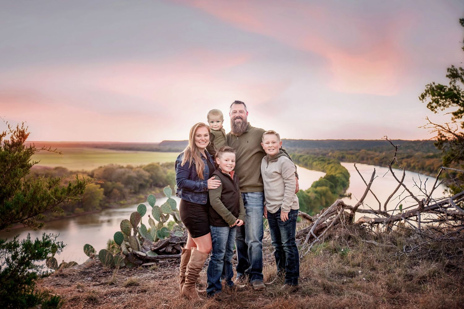 Small group poses on rocky overlook with river and sunset view in background.