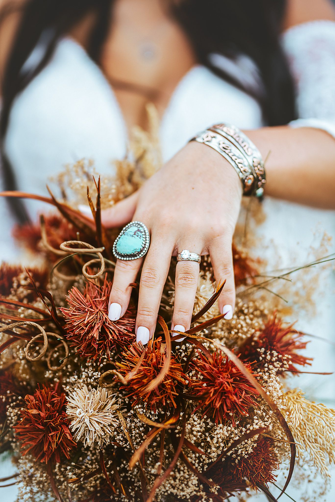 Turquoise ring and silver bangles accent dried flower bouquet with rustic autumn colors.