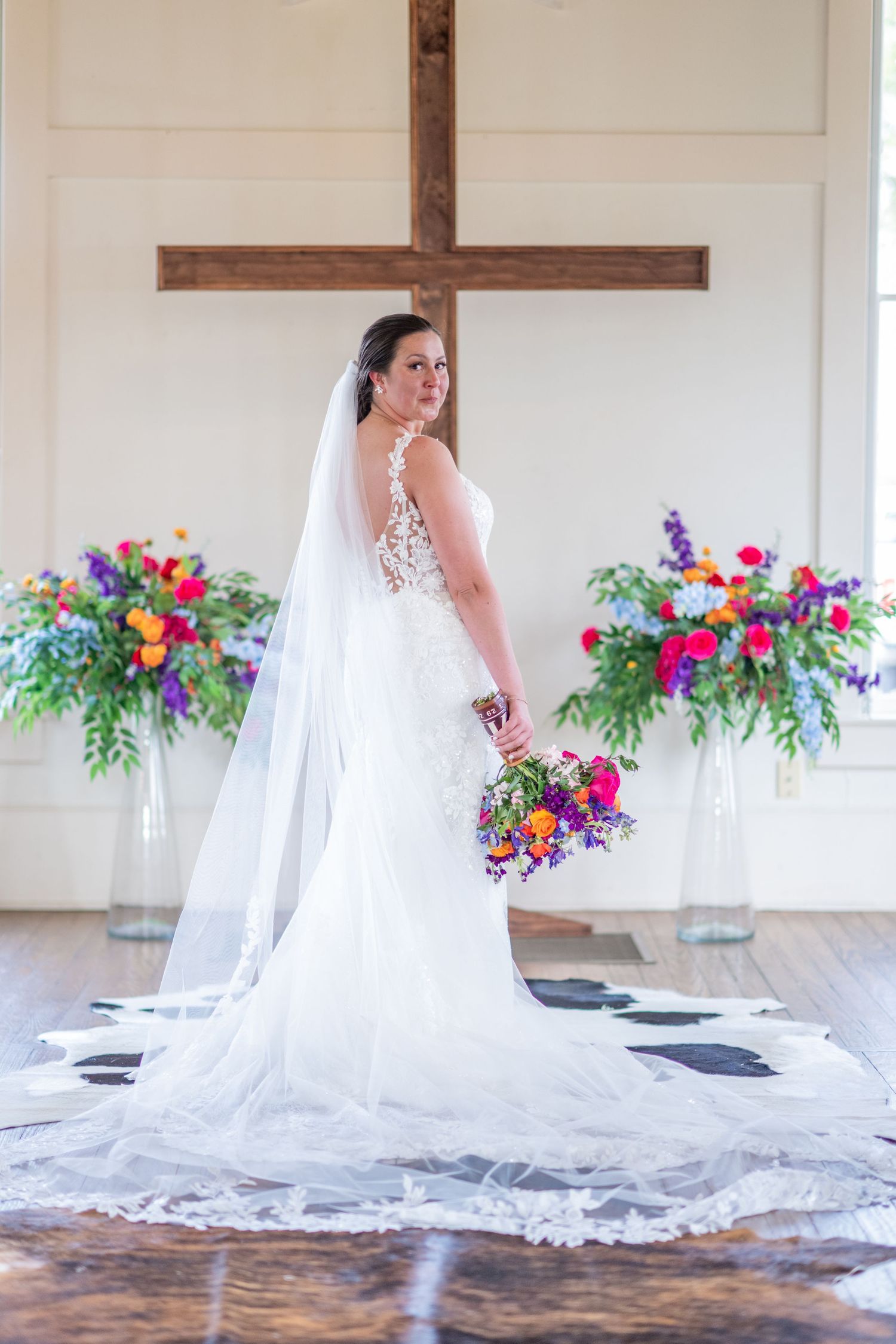 Wedding dress with dramatic cathedral veil displayed with vibrant floral arrangements.