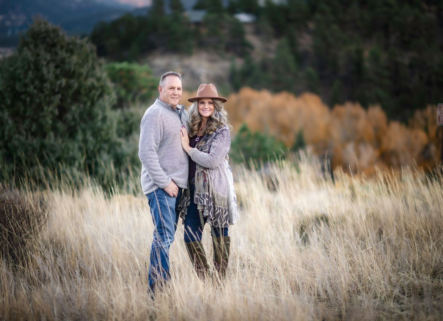Couple walking through tall grass field at sunset with golden light filtering through.