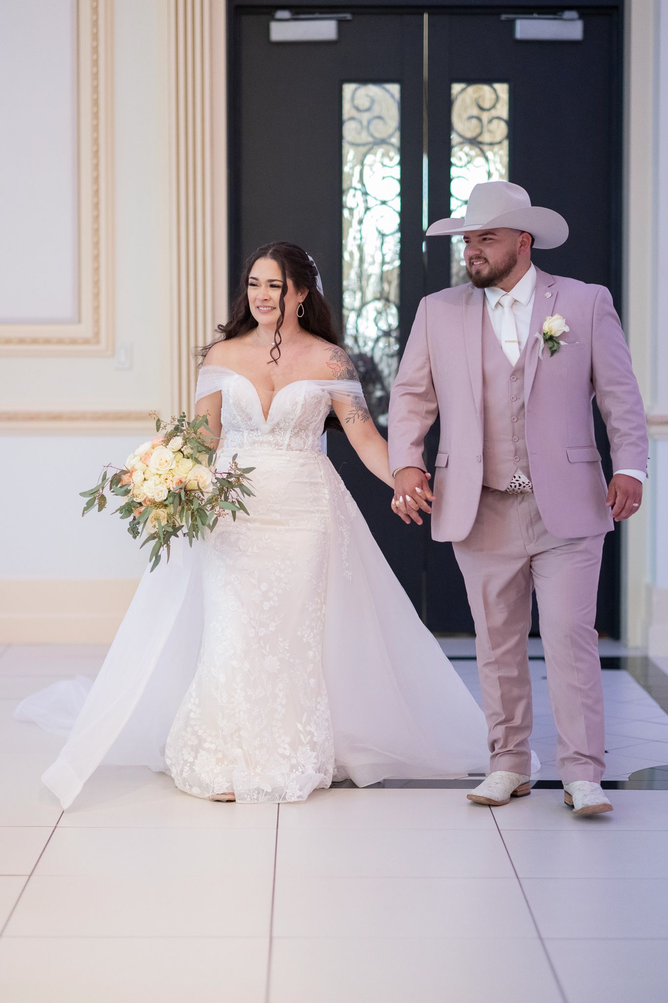 Newlyweds exit their ceremony, with the groom in a pink suit and cowboy hat.