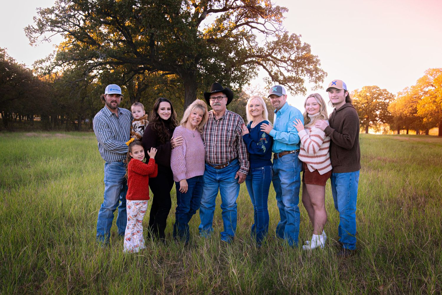 Large family group poses together in field during sunset photography session.