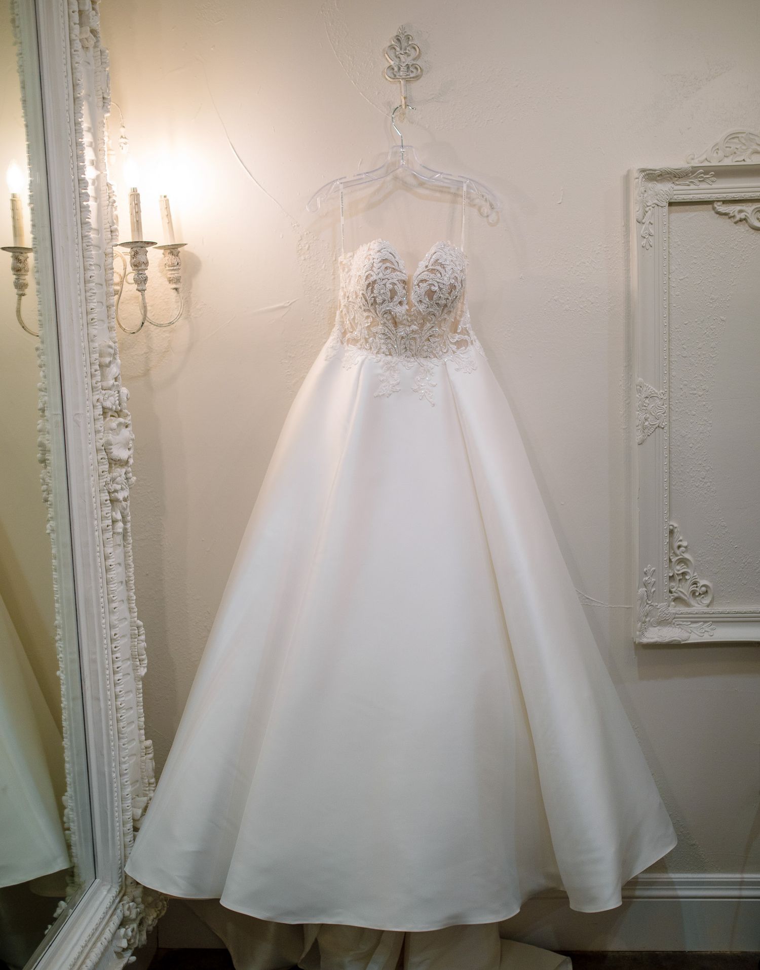 White ballgown wedding dress with beaded bodice displayed in elegant dressing room with ornate mirrors.