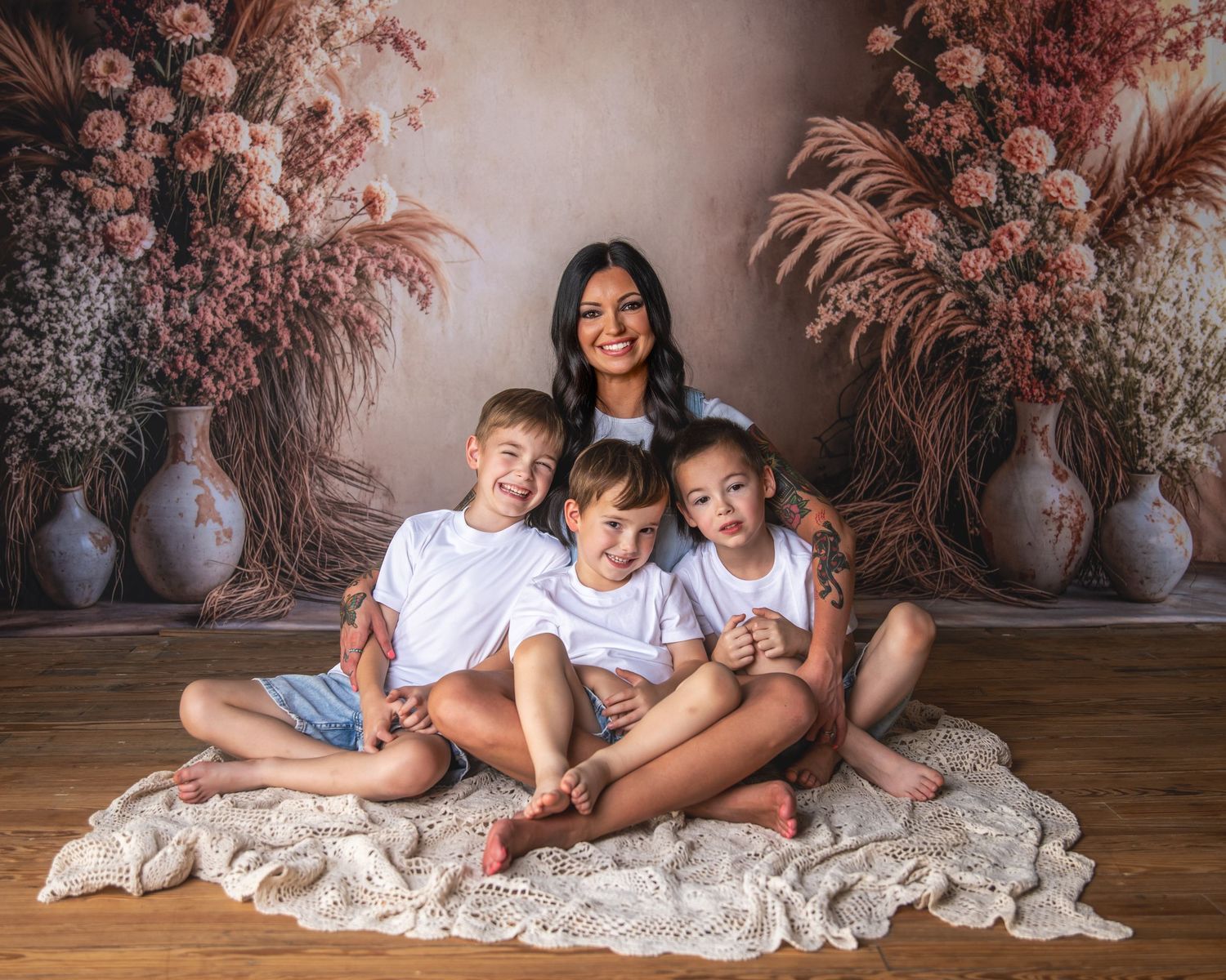 Children sitting together on a cream blanket against a floral backdrop in a studio setting.