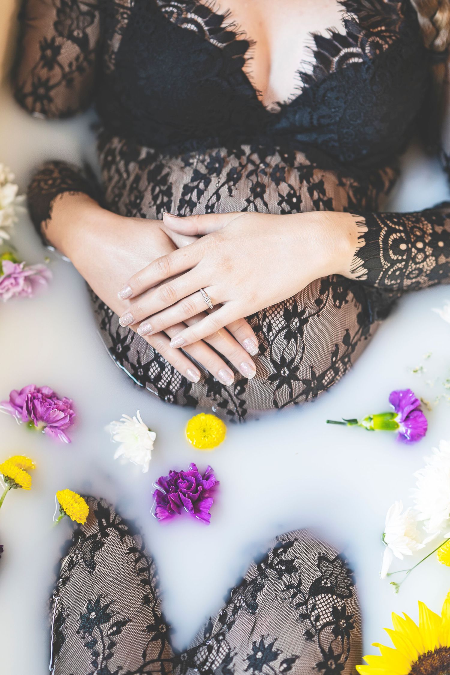 Maternity photo with black lace dress and scattered colorful flowers on white background.