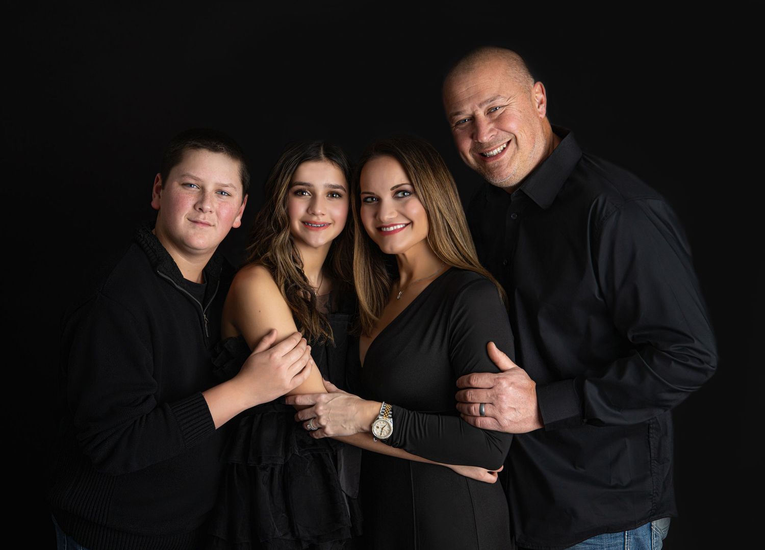 Professional studio portrait session featuring a family in black outfits against dark backdrop.