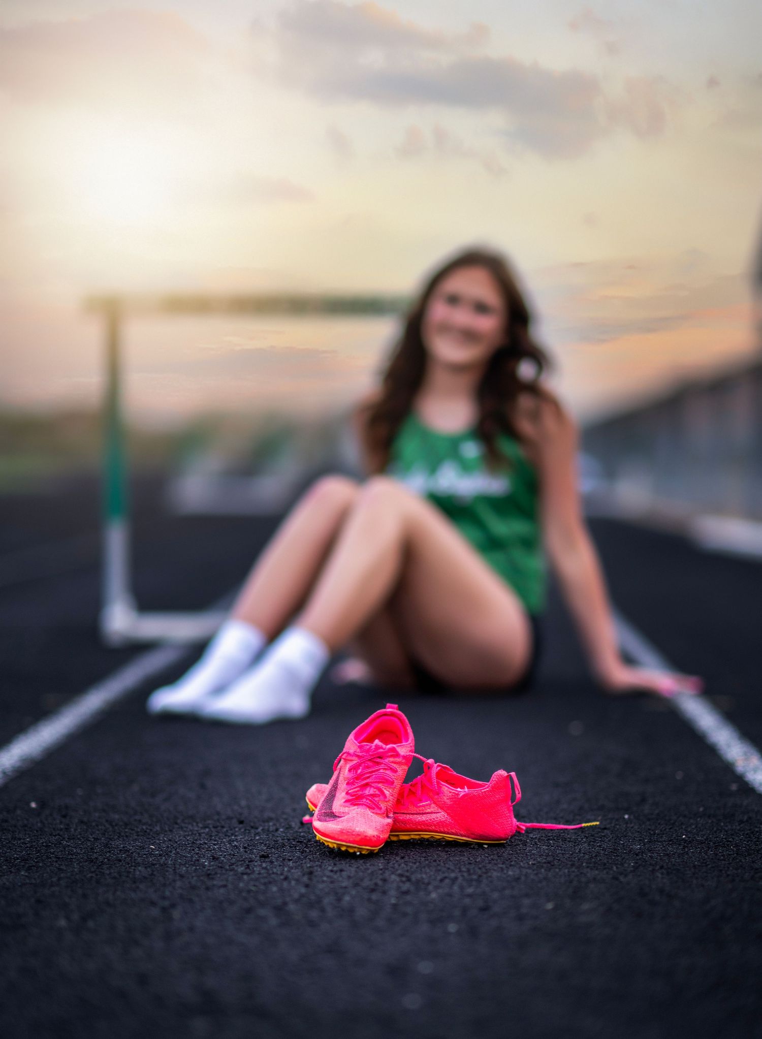 Artistic track and field photo with pink shoes in focus against blurred background at sunset.