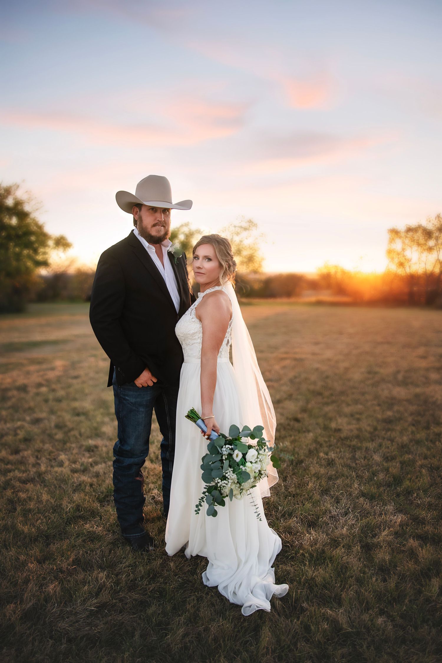 A rustic wedding photoshoot in a field at sunset capturing romantic moments.
