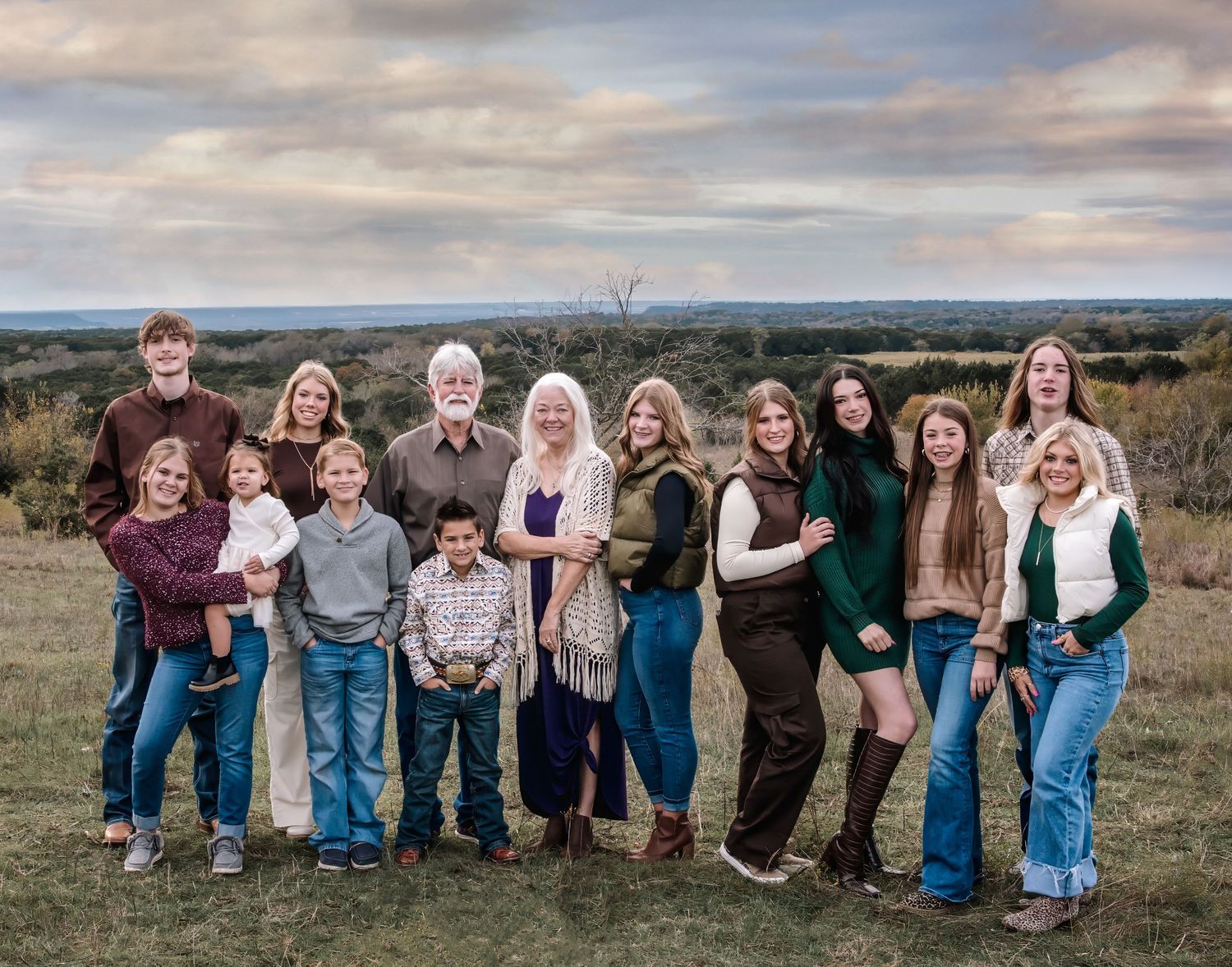 A group of people lined up outdoors posing playfully against a cloudy sky in a natural setting.