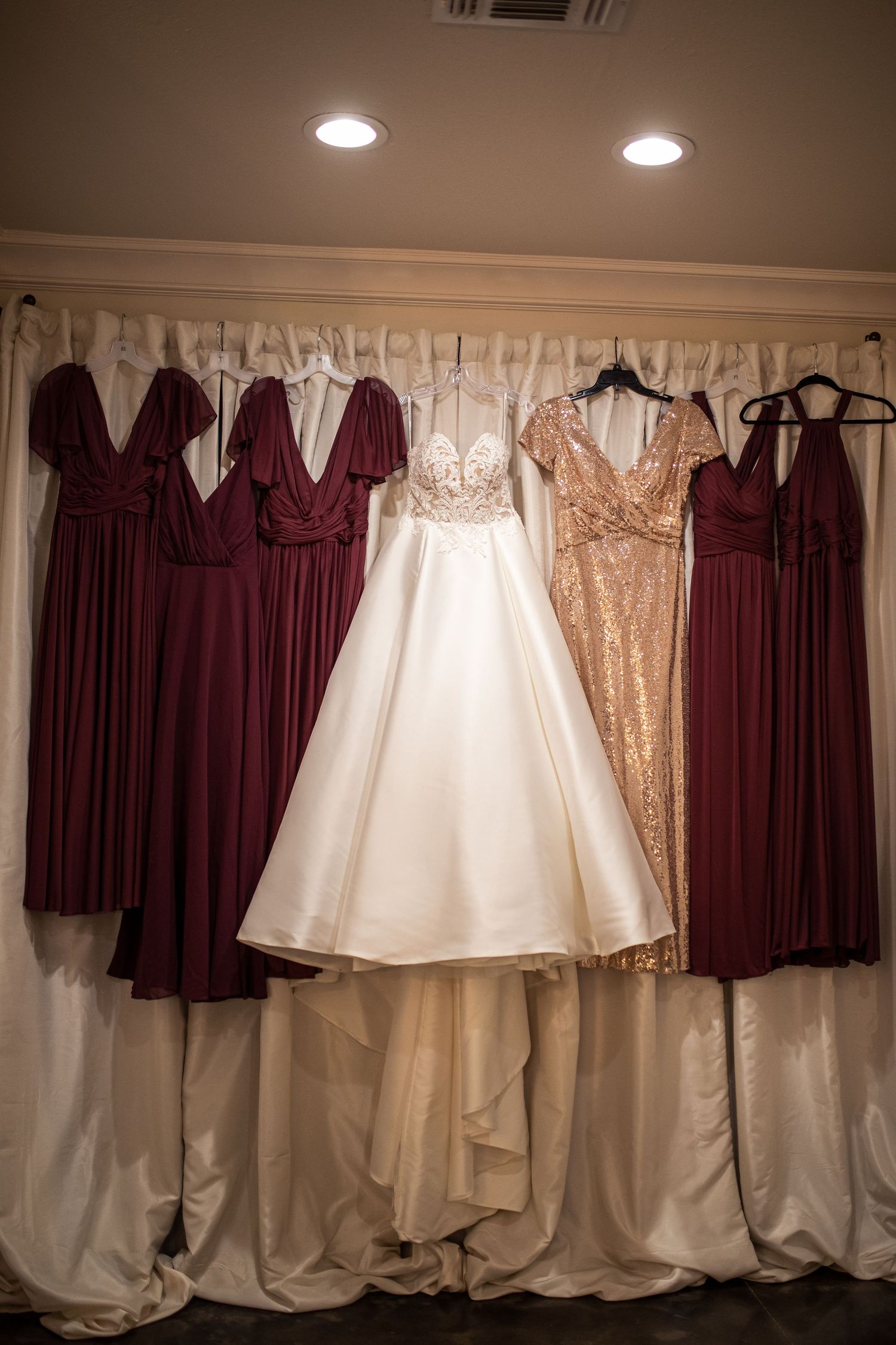 Wedding party dresses hanging including burgundy bridesmaid gowns and white bridal gown.