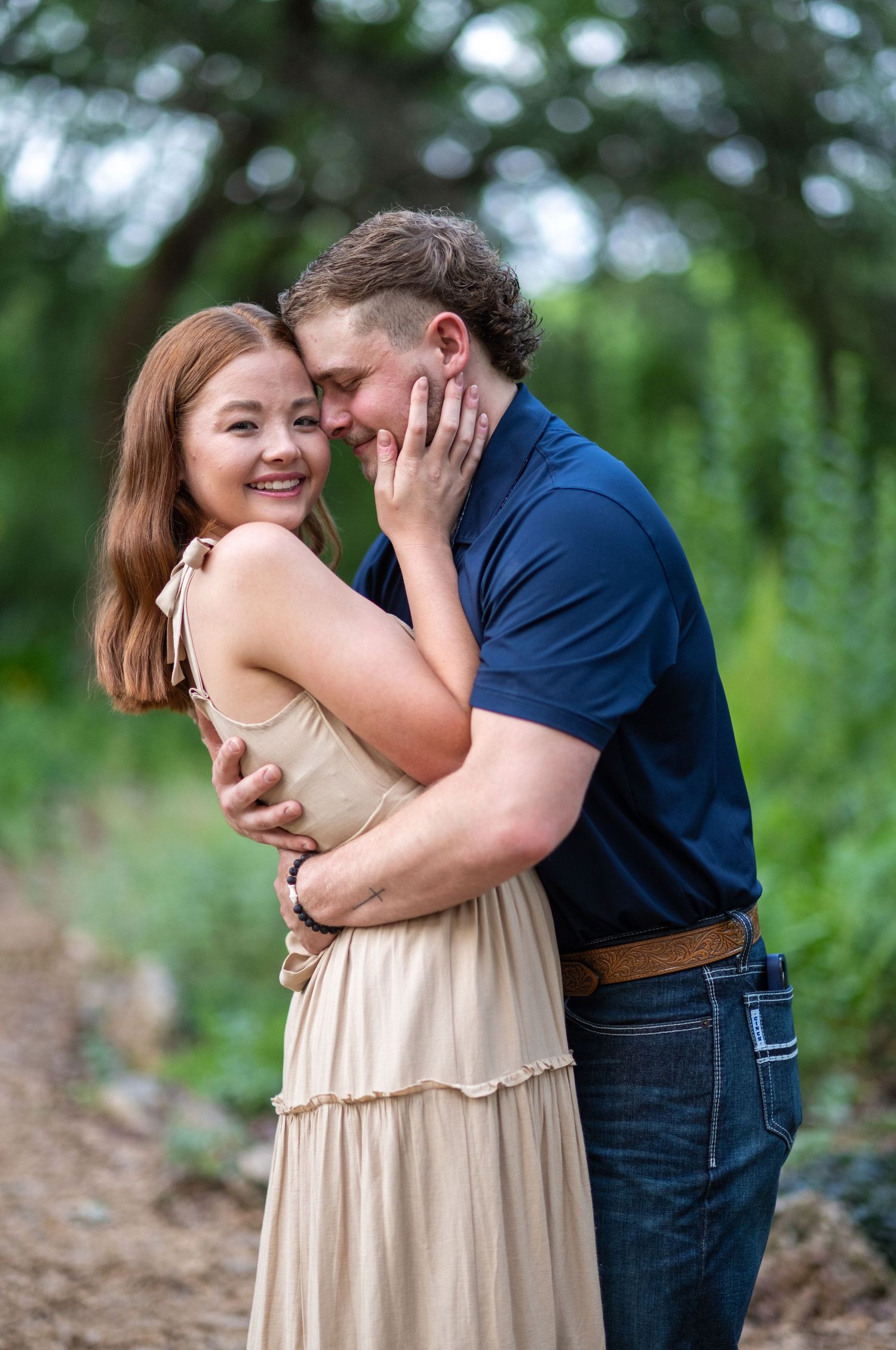 Romantic couple embracing outdoors in casual attire against a blurred natural background.
