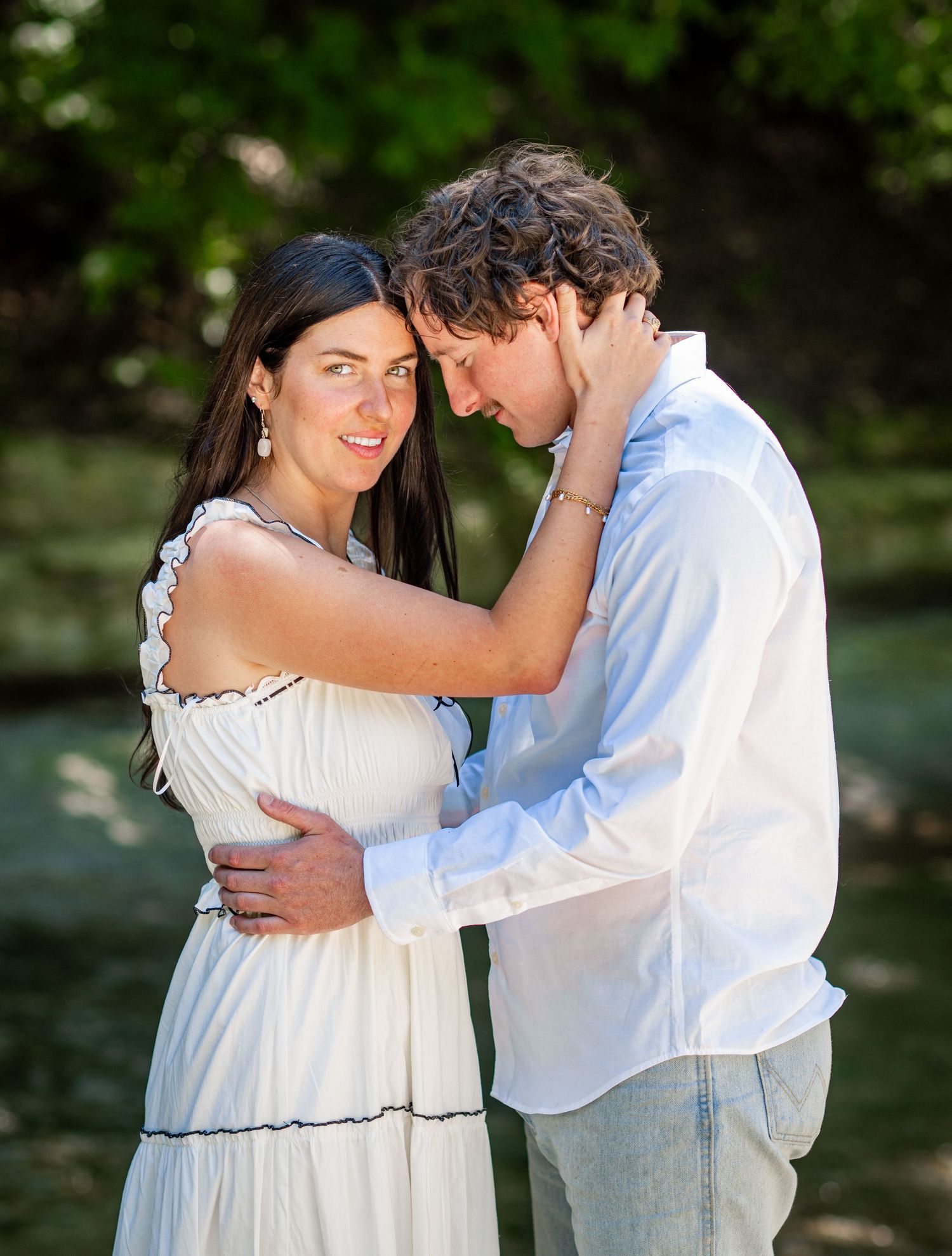 Intimate moment between couple in white clothing during outdoor photoshoot.