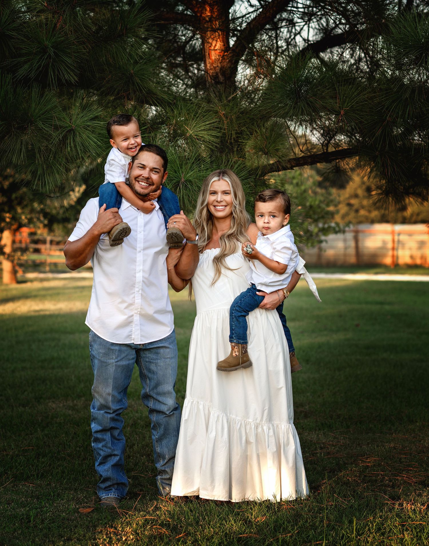 Family portrait series in white outfits playing together in a sunlit grassy field.