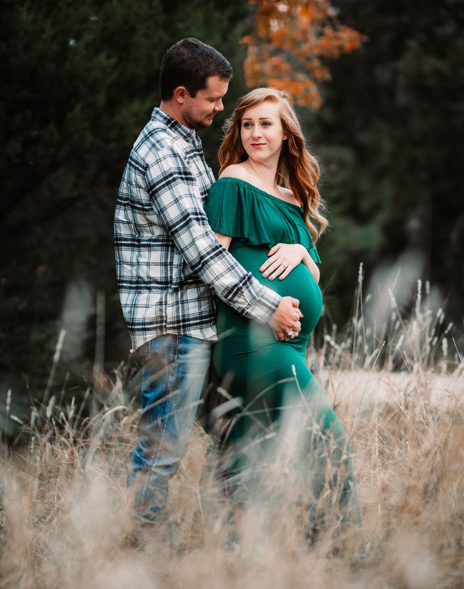 Expecting couple poses intimately in rustic field during sunset maternity session.