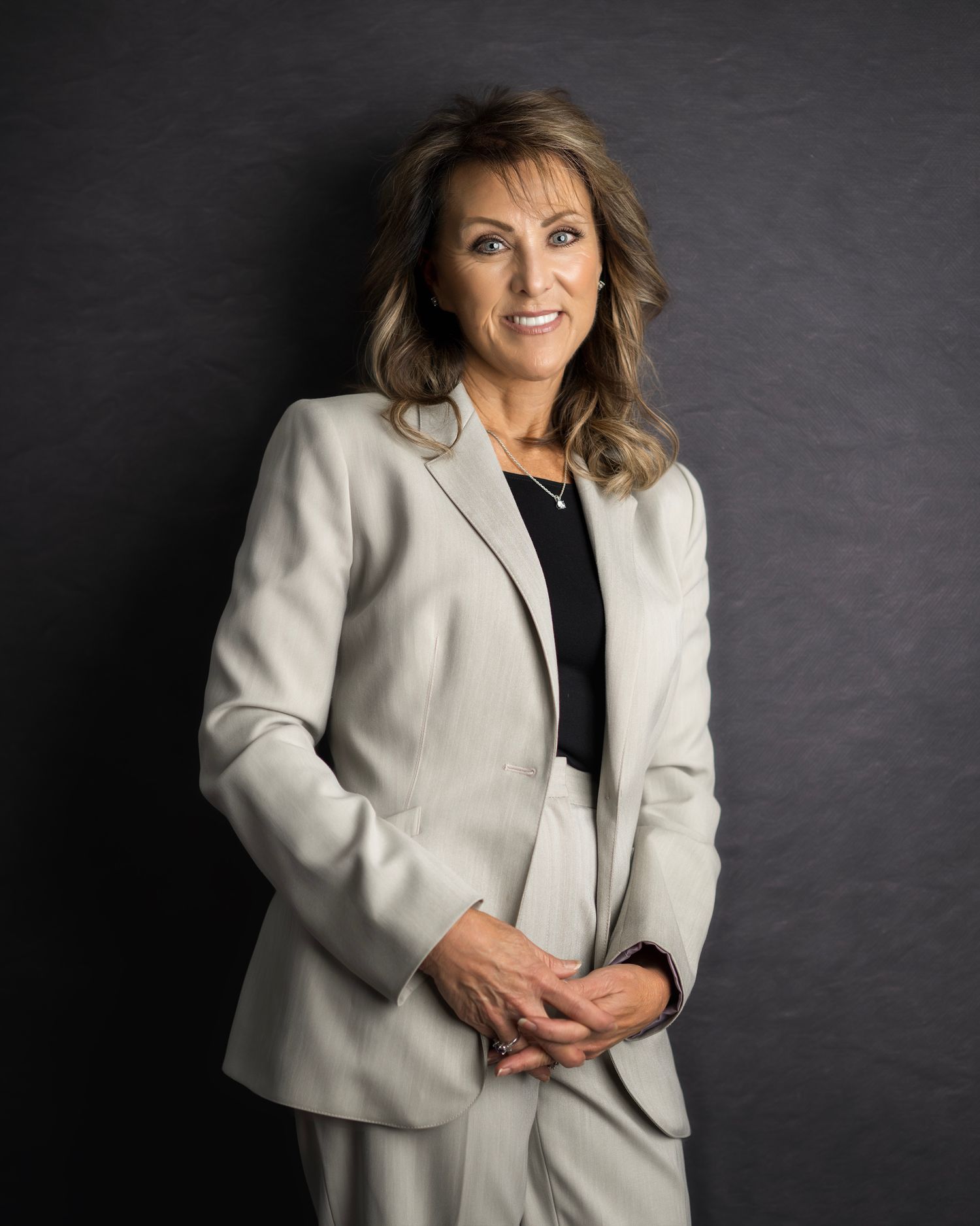 Professional headshot series against dark background wearing white blazer.
