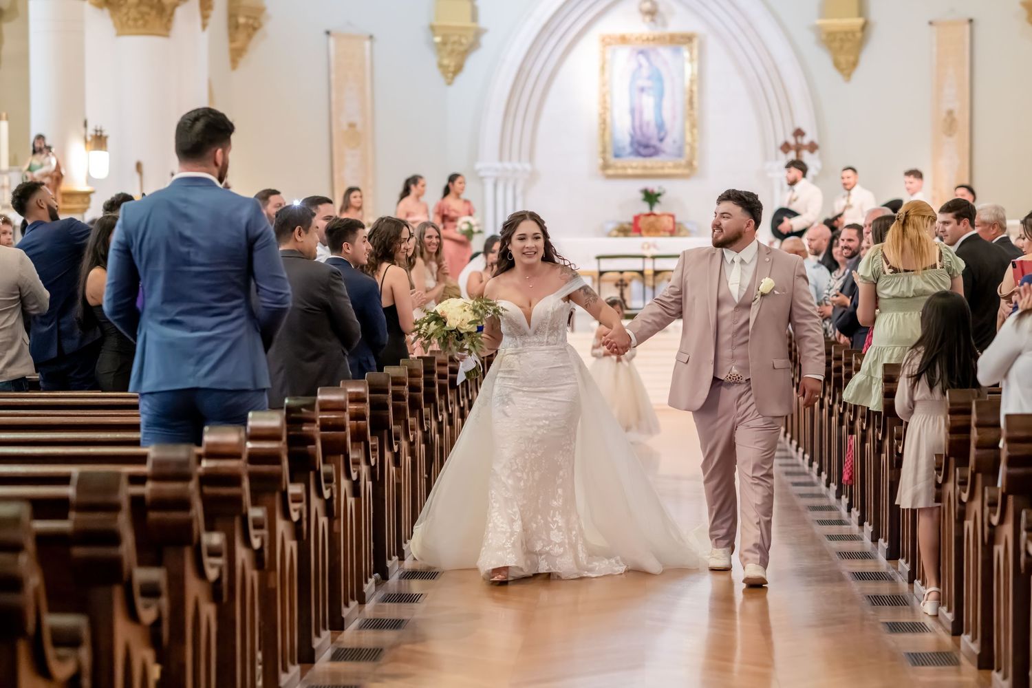 Joyful couple walking down church aisle during wedding ceremony recessional.