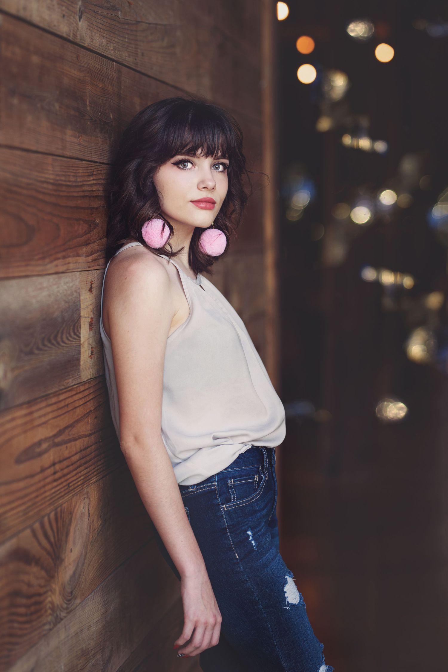Urban nighttime portrait against wooden wall with bokeh lights in background.
