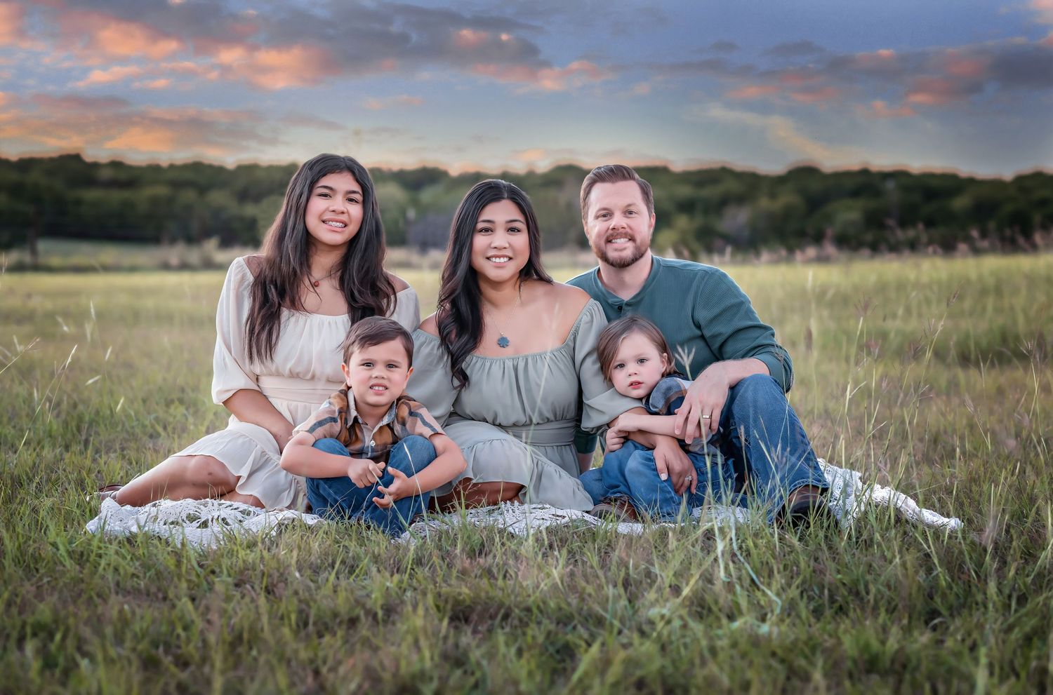 Family seated on blanket in grassy field during sunset photoshoot.