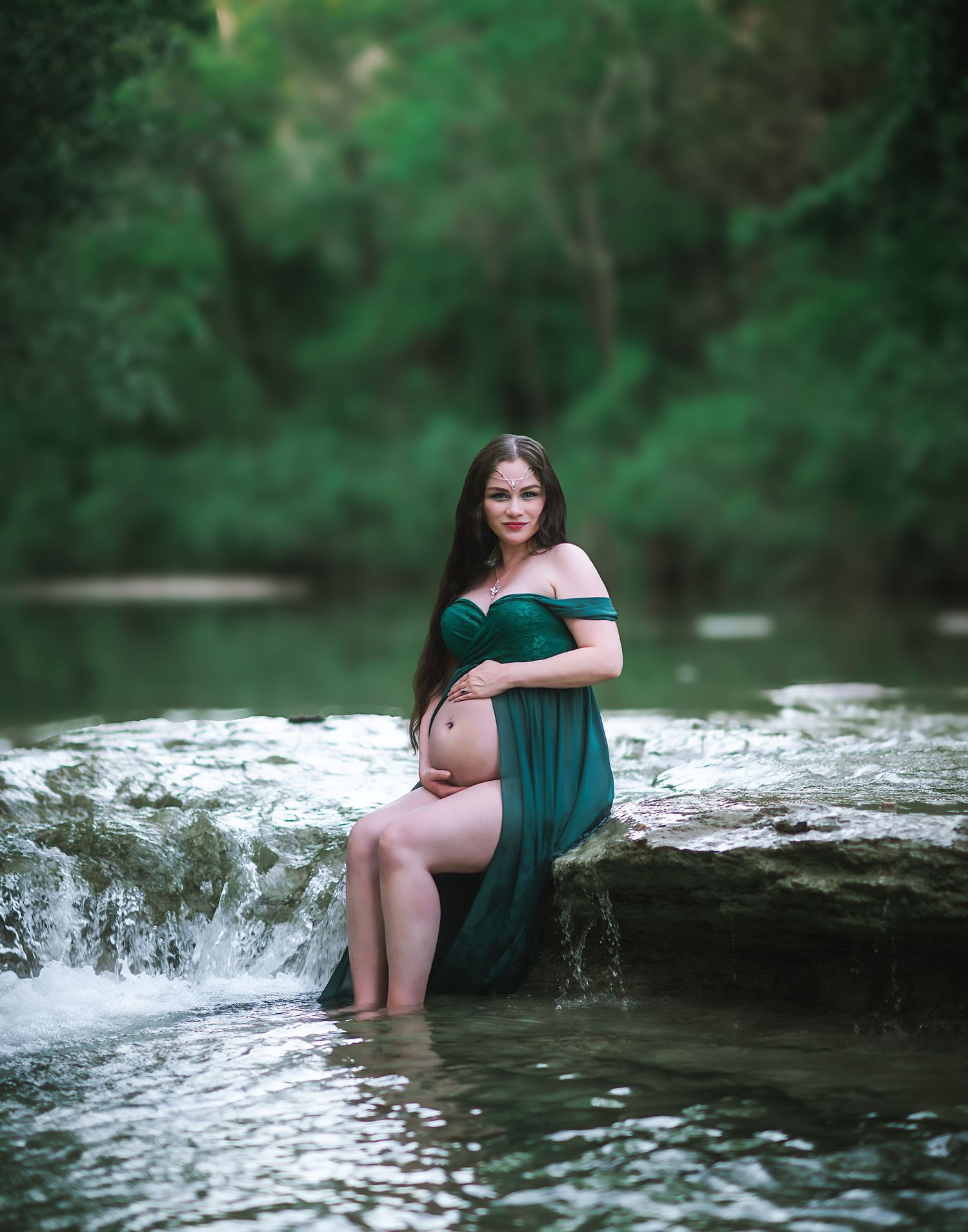 Peaceful maternity moment captured at waterfall's edge in flowing green dress.