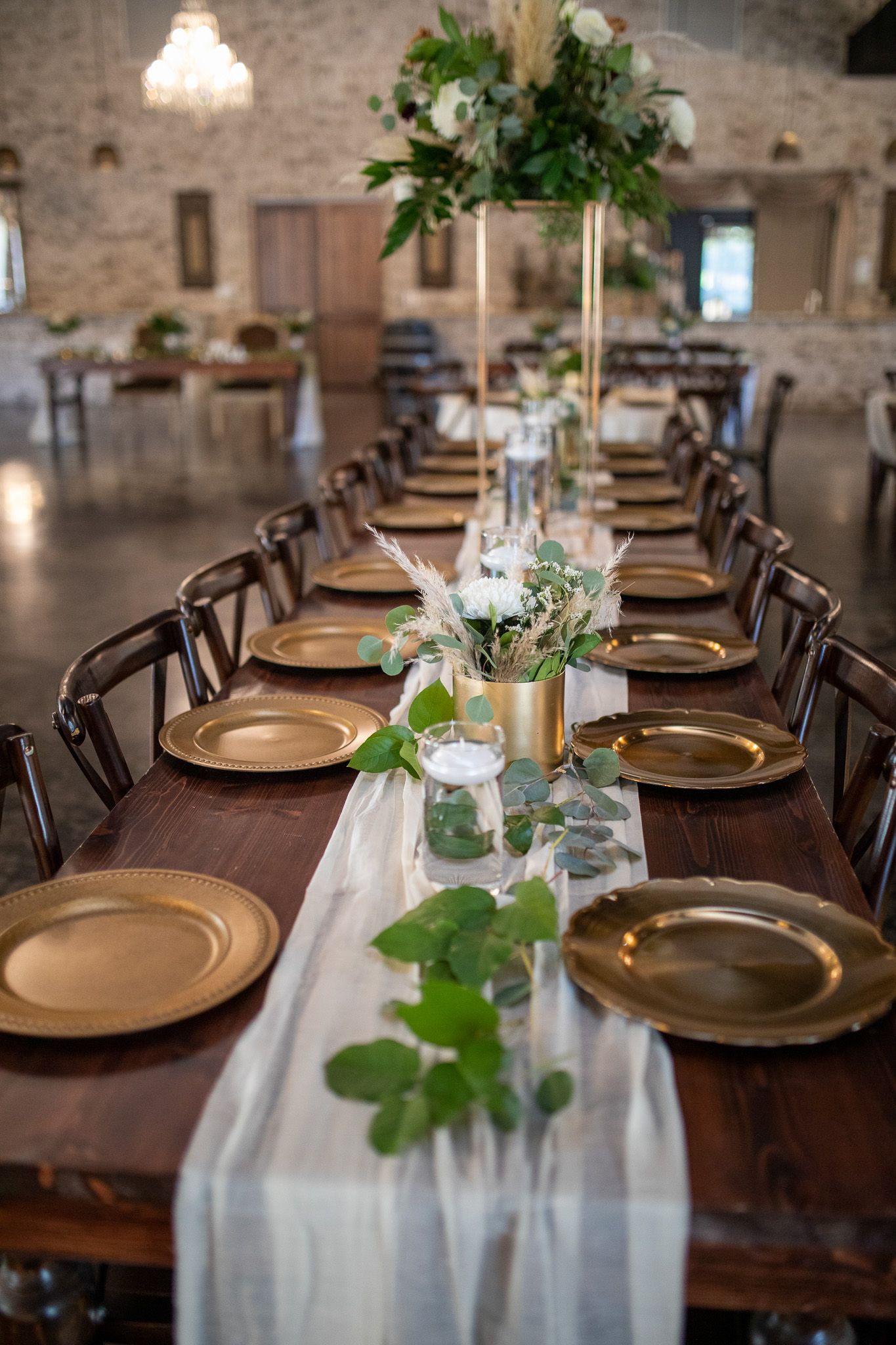 Long dining tables decorated with white linens, place settings and delicate floral centerpieces in a rustic venue.