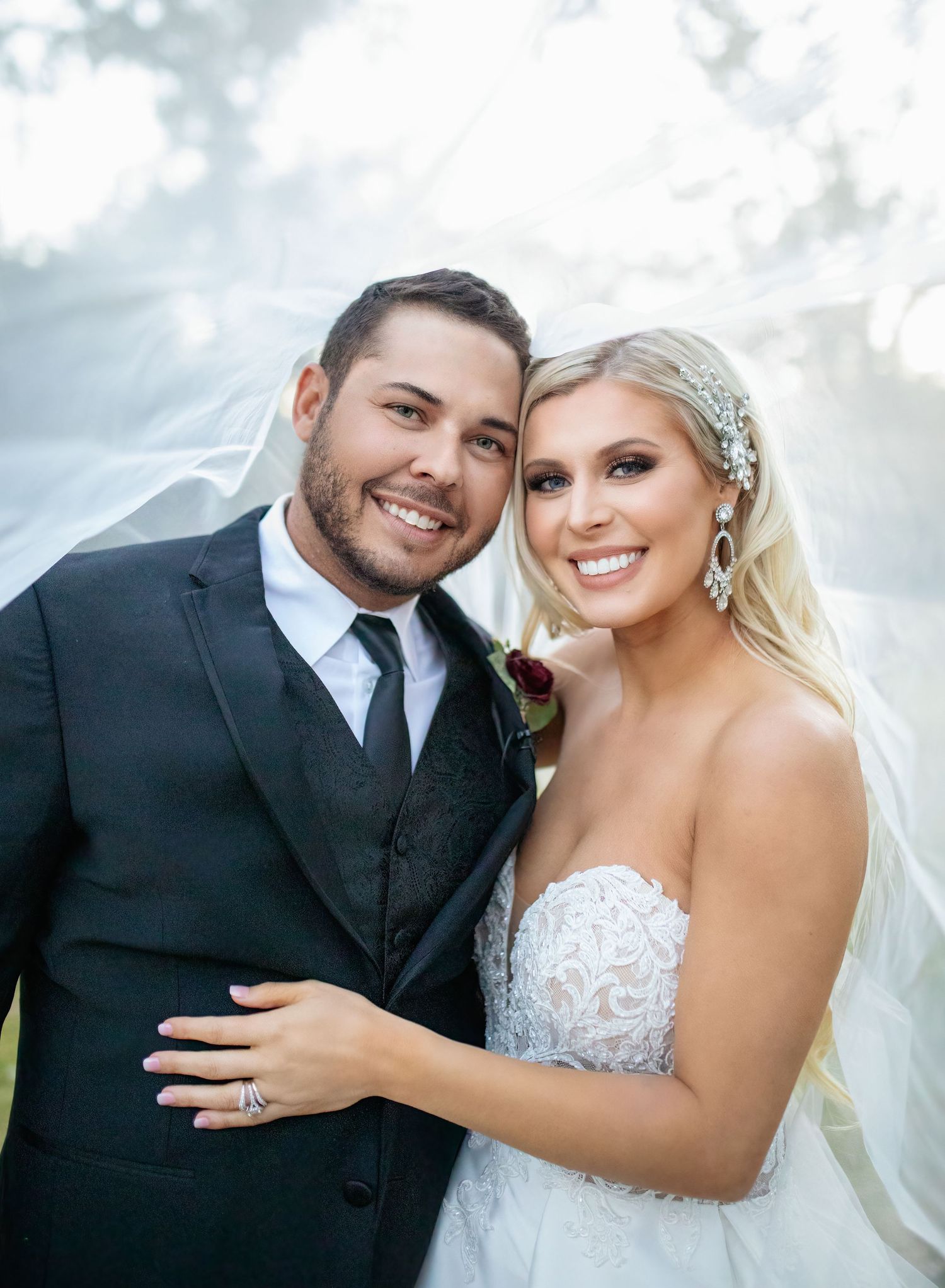 A happy wedding couple poses together outdoors with soft bokeh lighting in the background.