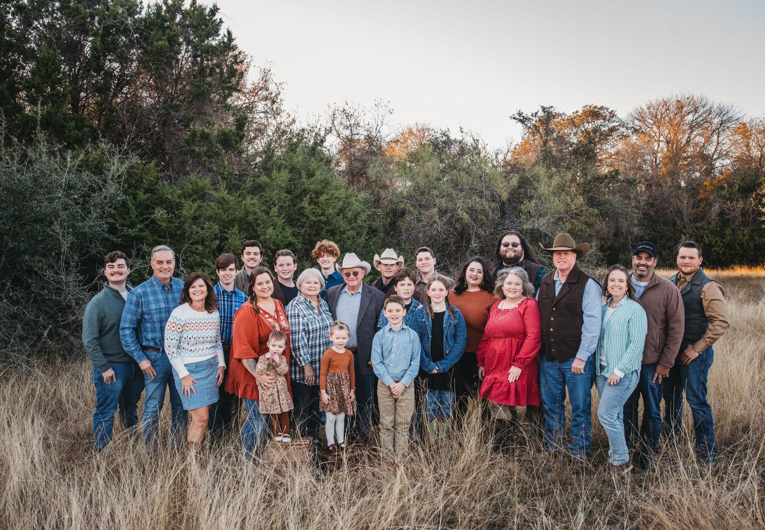 Large group photo of wedding party and guests posed in autumn field at sunset.