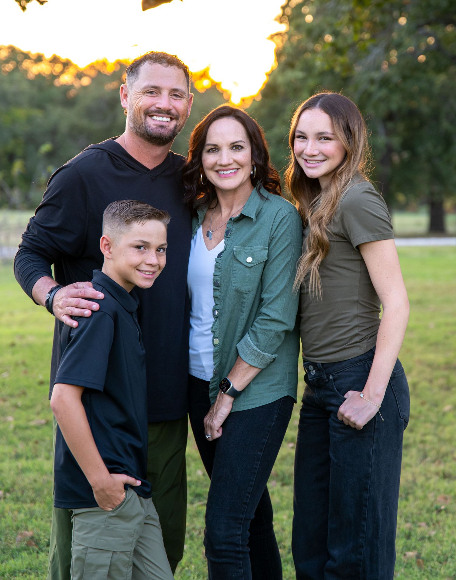 Family portrait in coordinating green and black casual outfits with sunset backdrop.