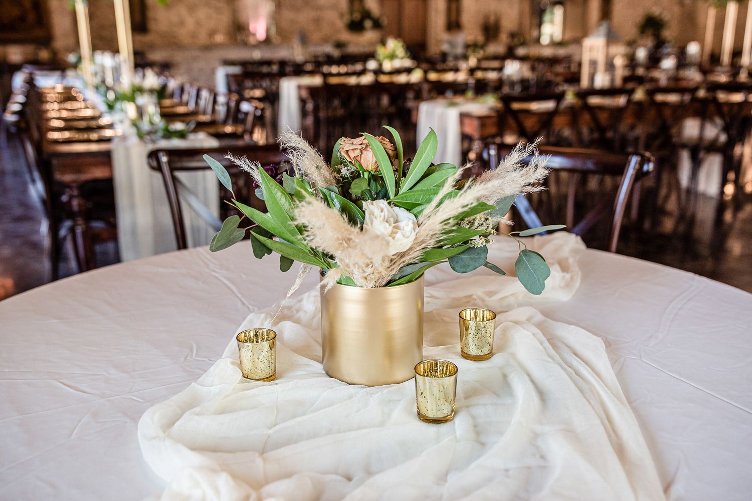 Elegant wedding centerpiece with gold vase, greenery and white florals on white tablecloth.