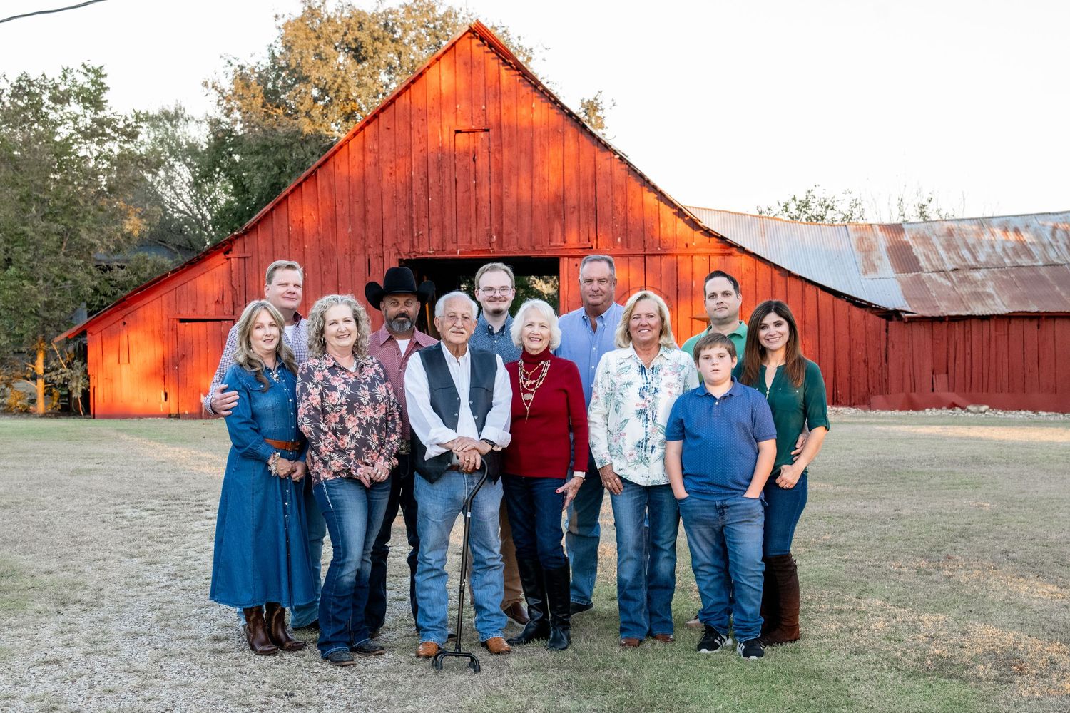 Large group portrait in front of a rustic red barn in casual western attire.