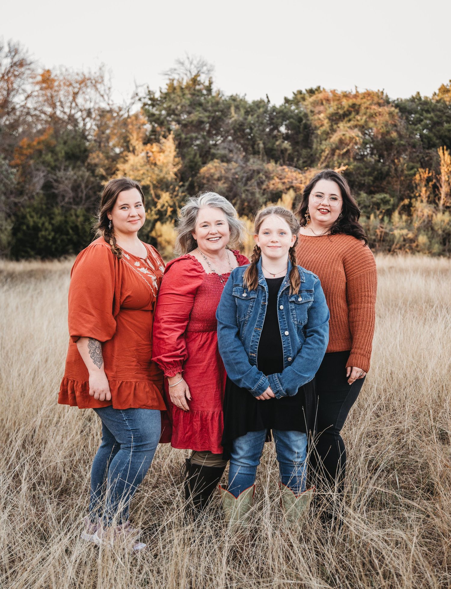 People wearing autumn colors pose together in tall grass during golden hour.