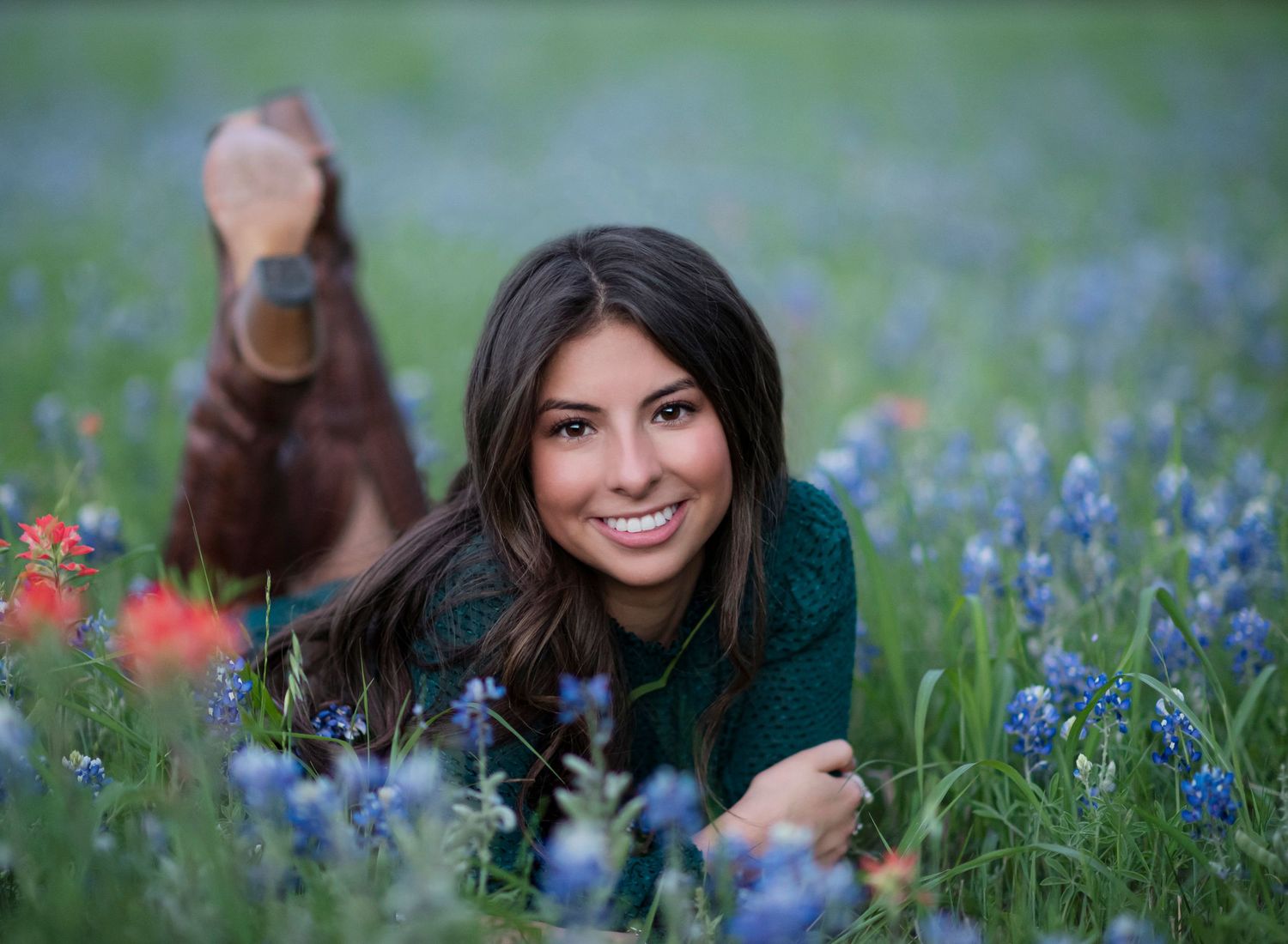 Woman lying in a meadow of blue wildflowers and red poppies on a sunny spring day.