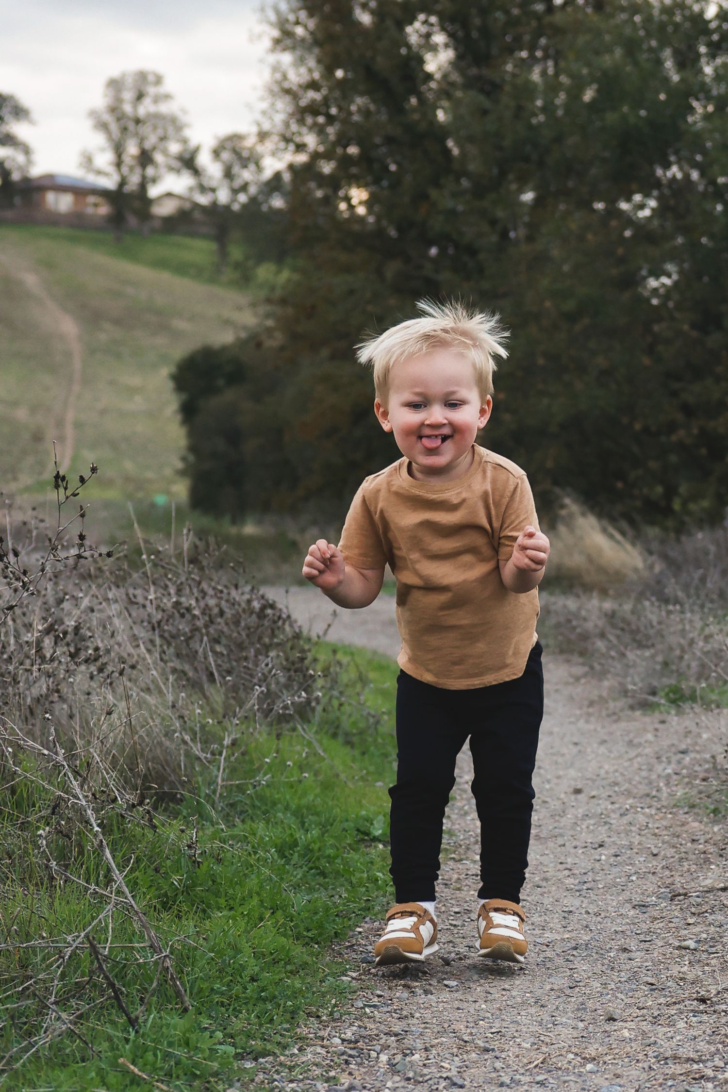 Child in brown sweater and dark pants plays energetically on a rural gravel path.