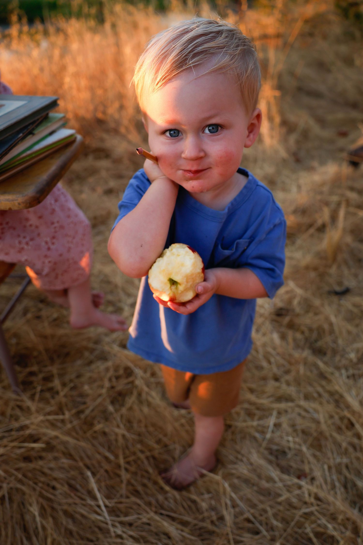 Child in blue shirt enjoys a snack while playing outdoors at sunset.