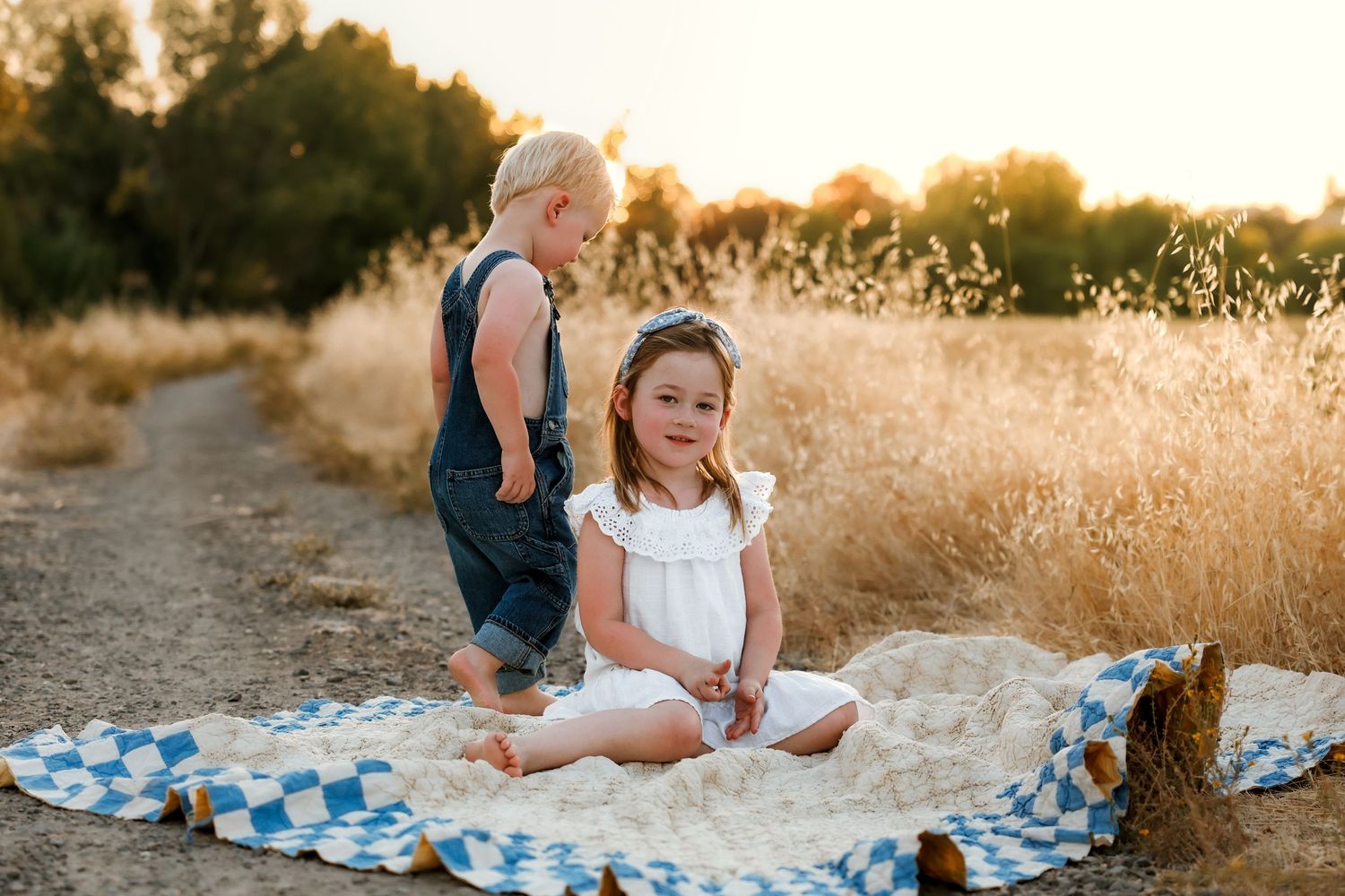 Playful outdoor family photoshoot in a sun-drenched field with blue checkered blanket.